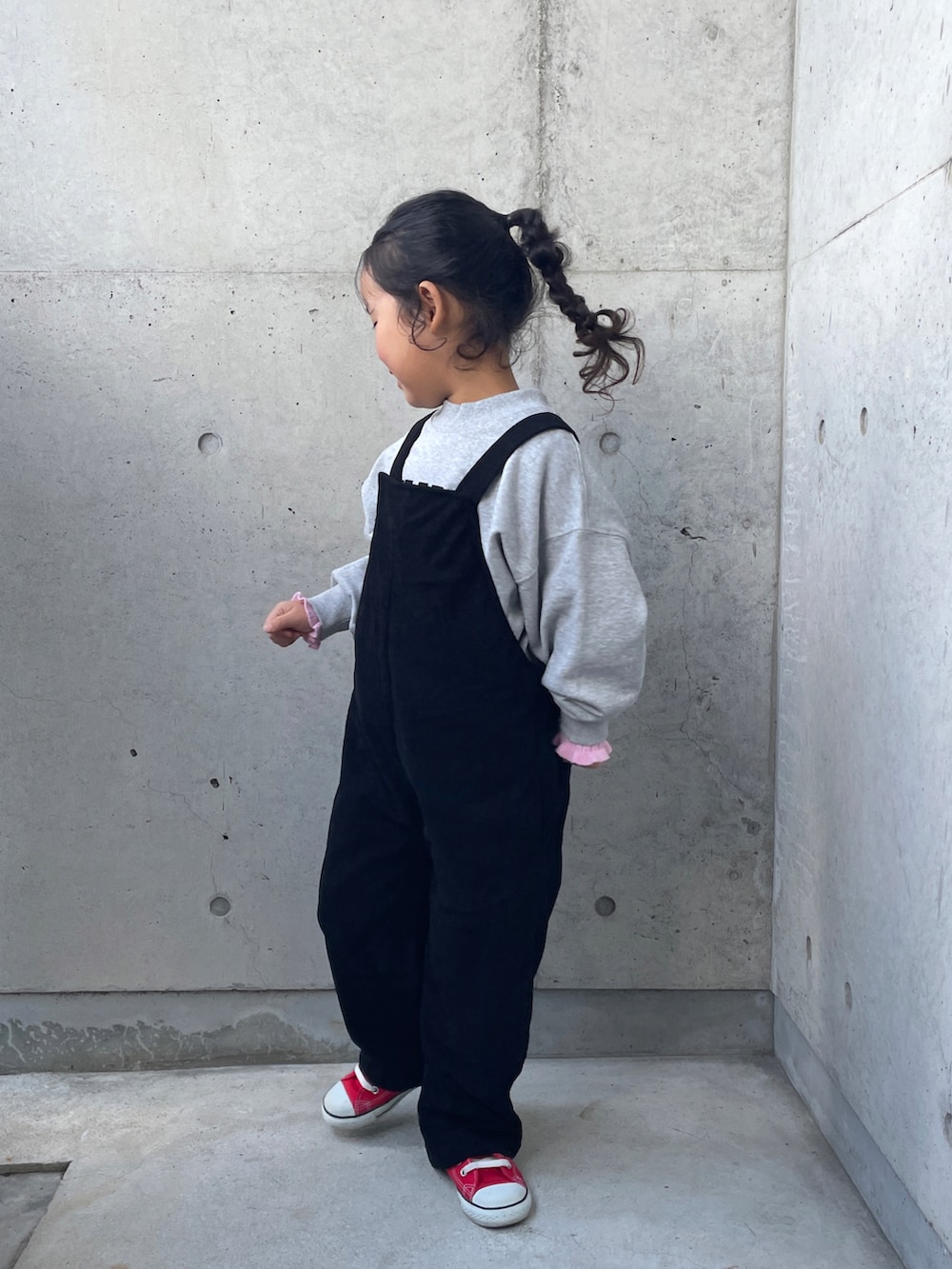 グレー系のスウェット、ブラック系のサロペット/オーバーオール、ピンク系のニット/セーターを着用したキッズの冬コーディネートの2枚目の写真