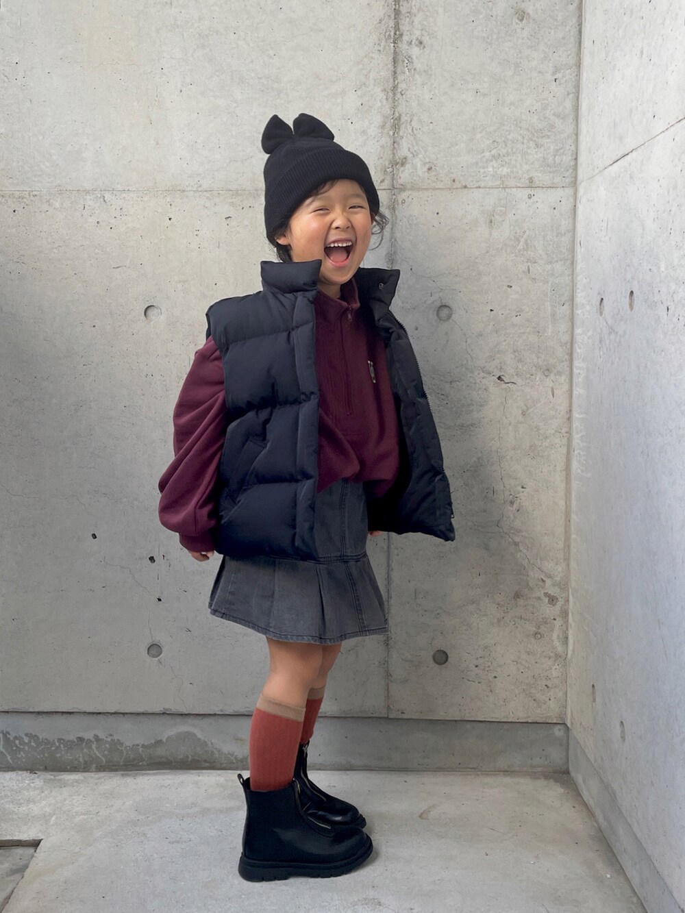 レッド系のスウェット、ブラック系のダウンベスト、ブラック系のブーツを着用したキッズの冬コーディネートの2枚目の写真