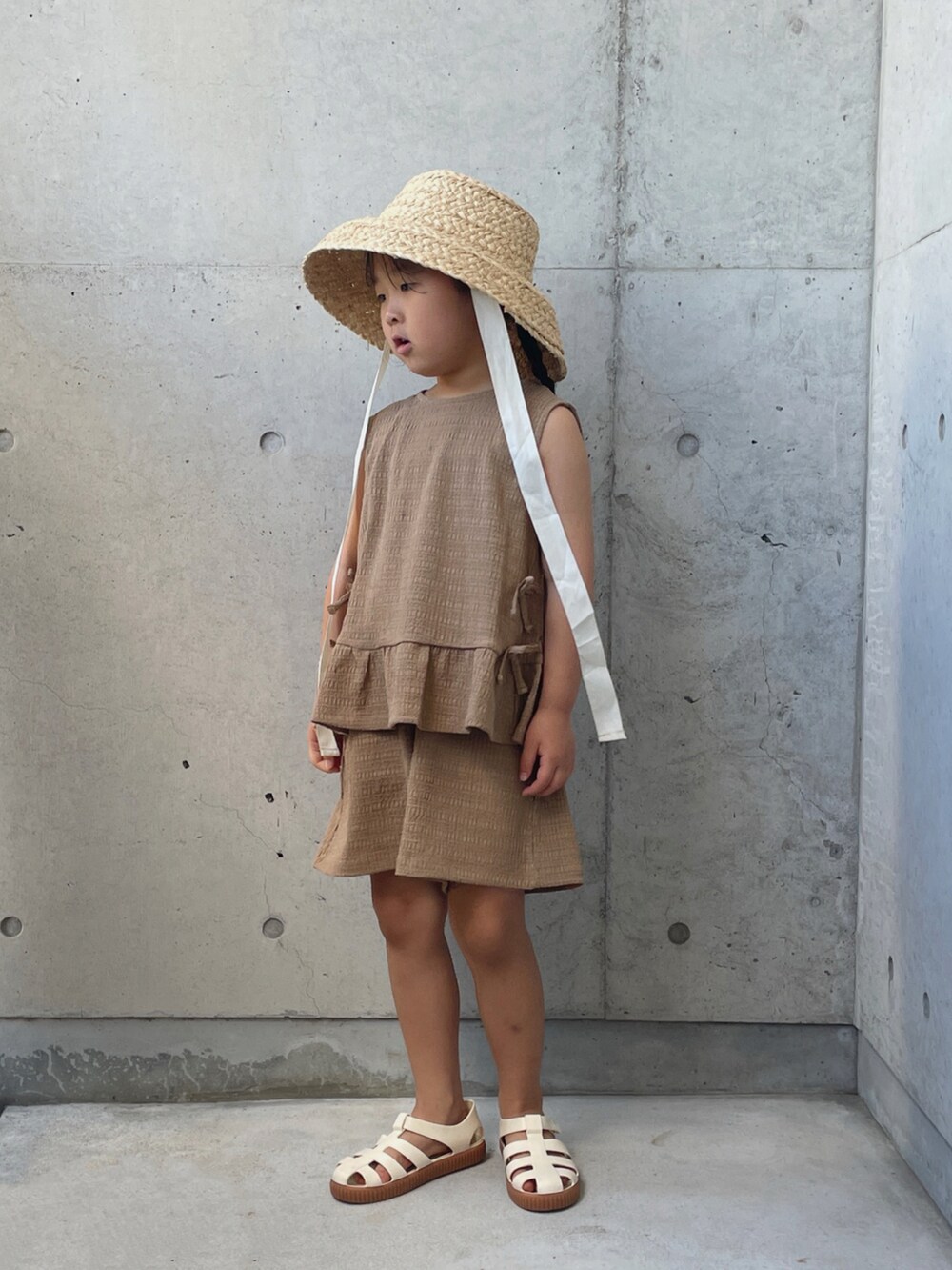 ブラウン系のパンツドレス、ホワイト系のサンダル、ホワイト系のハットを着用したキッズの夏コーディネートの5枚目の写真
