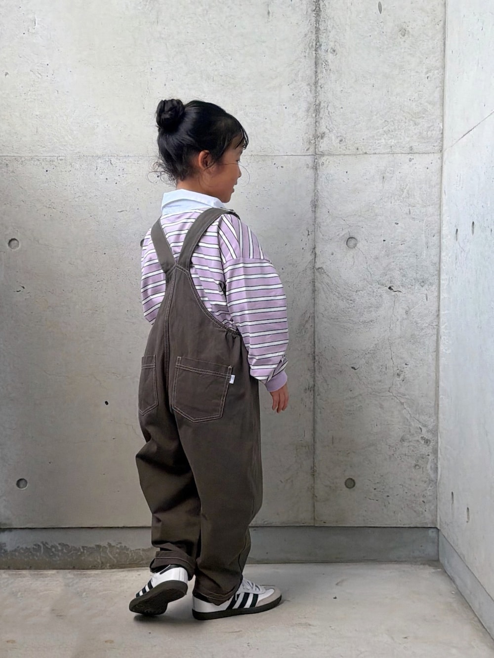 パープル系のポロシャツ、ホワイト系のスニーカー、グレー系のサロペット/オーバーオールを着用したキッズの秋コーディネートの5枚目の写真