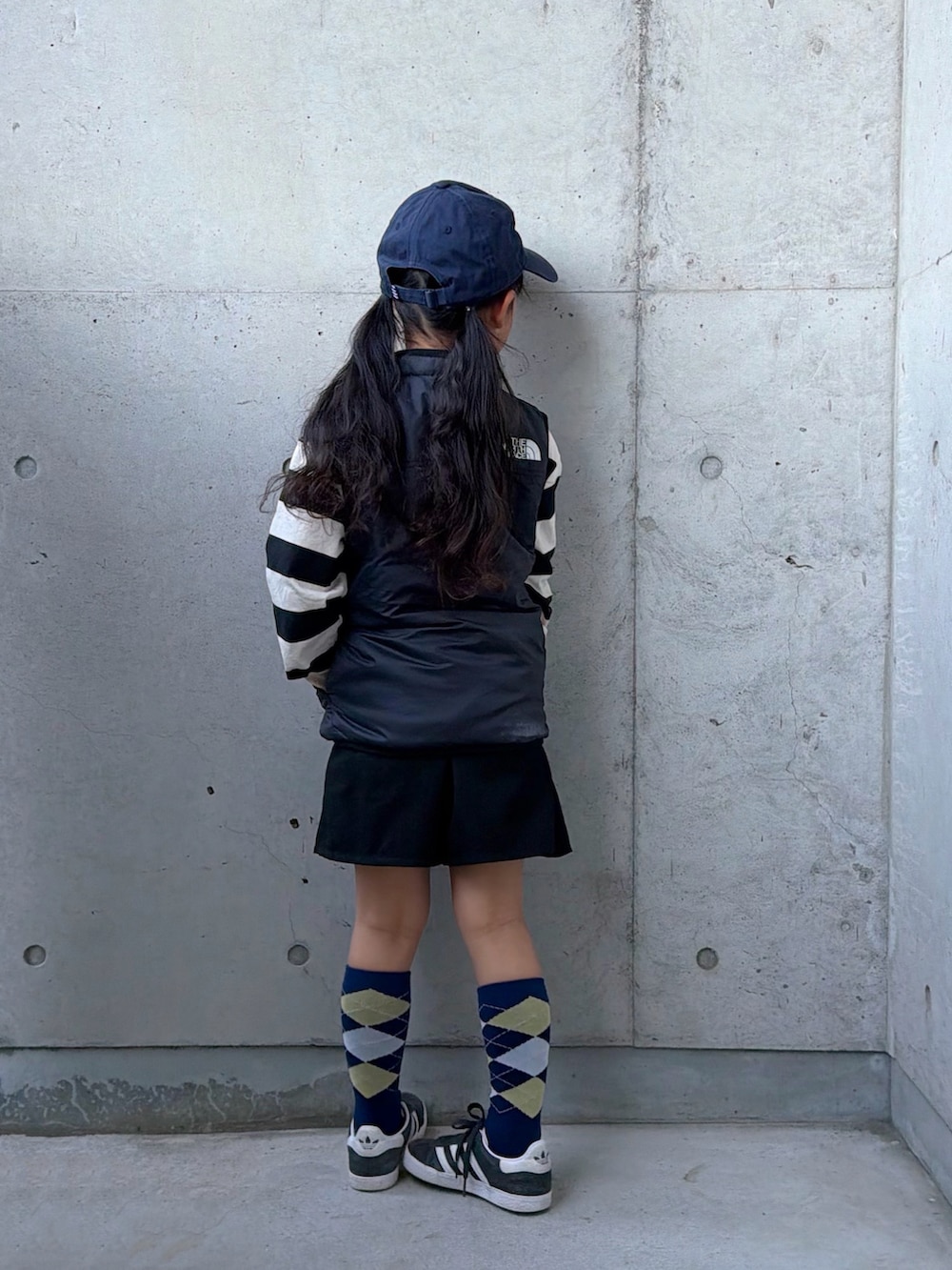 ブラック系のベスト、ホワイト系のポロシャツ、ベージュ系のスカートを着用したキッズの冬コーディネートの3枚目の写真