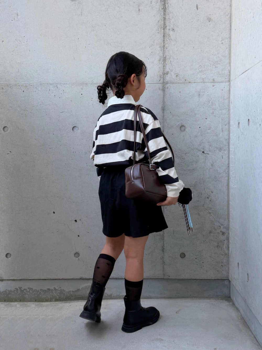 ブラウン系のショルダーバッグ、ブラック系のブーツ、ホワイト系のポロシャツを着用したキッズの秋コーディネートの2枚目の写真