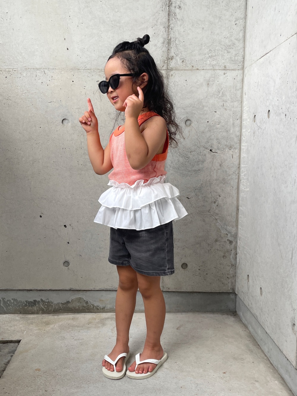 ホワイト系のサンダル、オレンジ系のタンクトップ、グレー系のパンツを着用したキッズの夏コーディネートの3枚目の写真