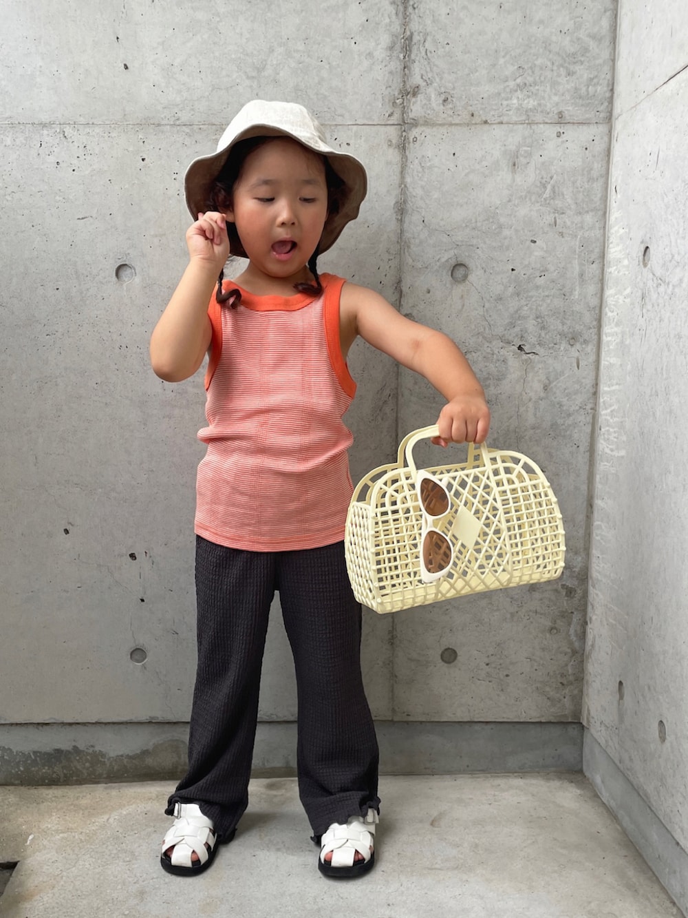 オレンジ系のタンクトップ、グレー系のその他パンツ、ホワイト系のバッグを着用したキッズの夏コーディネートの3枚目の写真