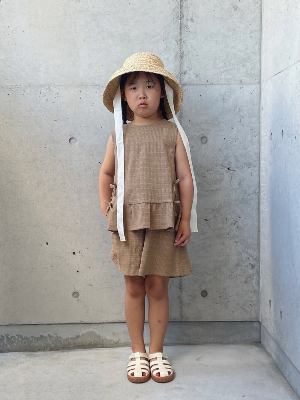 ブラウン系のパンツドレス、ホワイト系のサンダル、ホワイト系のハットを着用したキッズの夏コーディネートの3枚目の写真