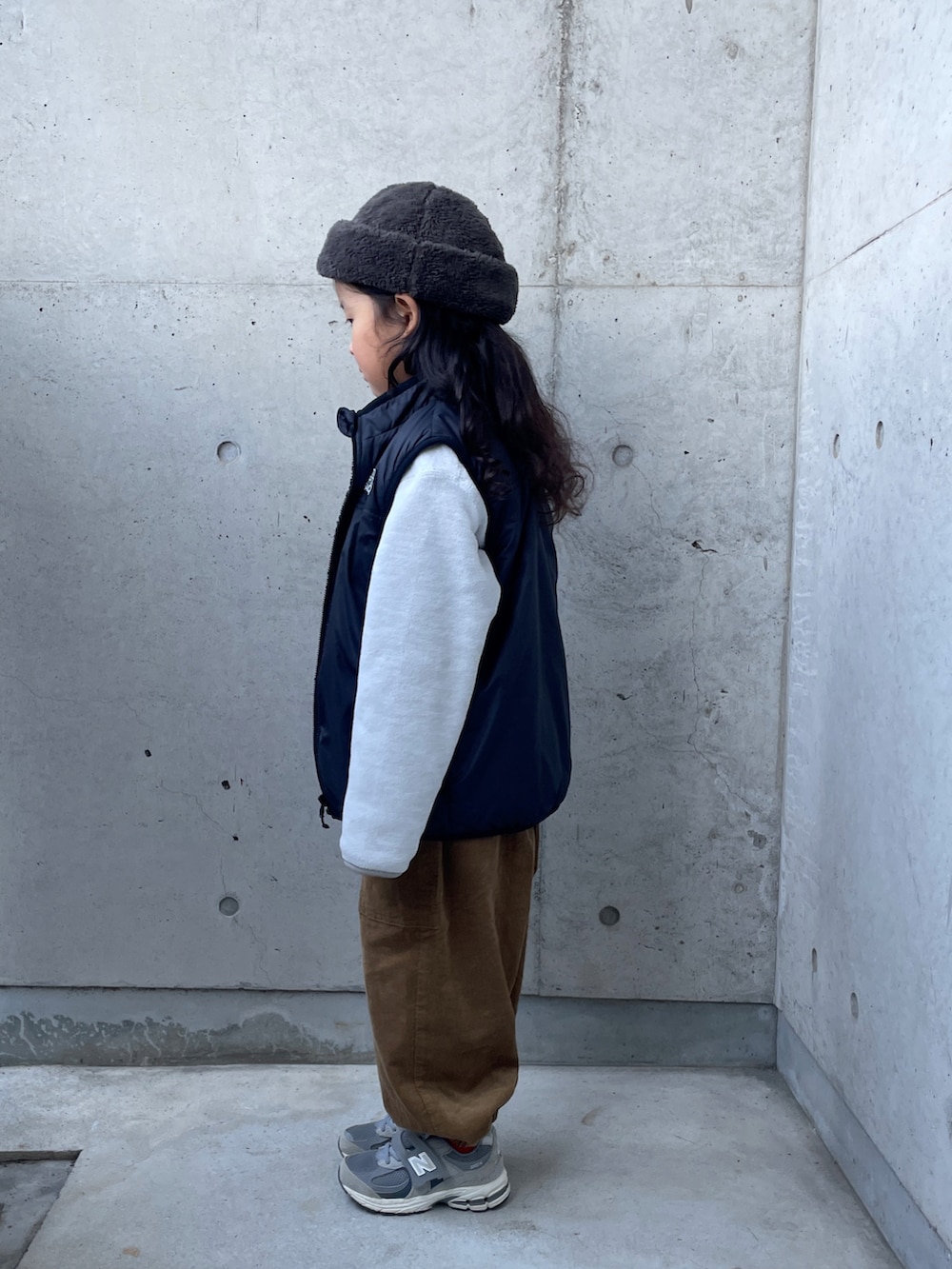 グレー系のトップス、ブラック系のベスト、イエロー系のその他パンツを着用したキッズの冬コーディネートの2枚目の写真