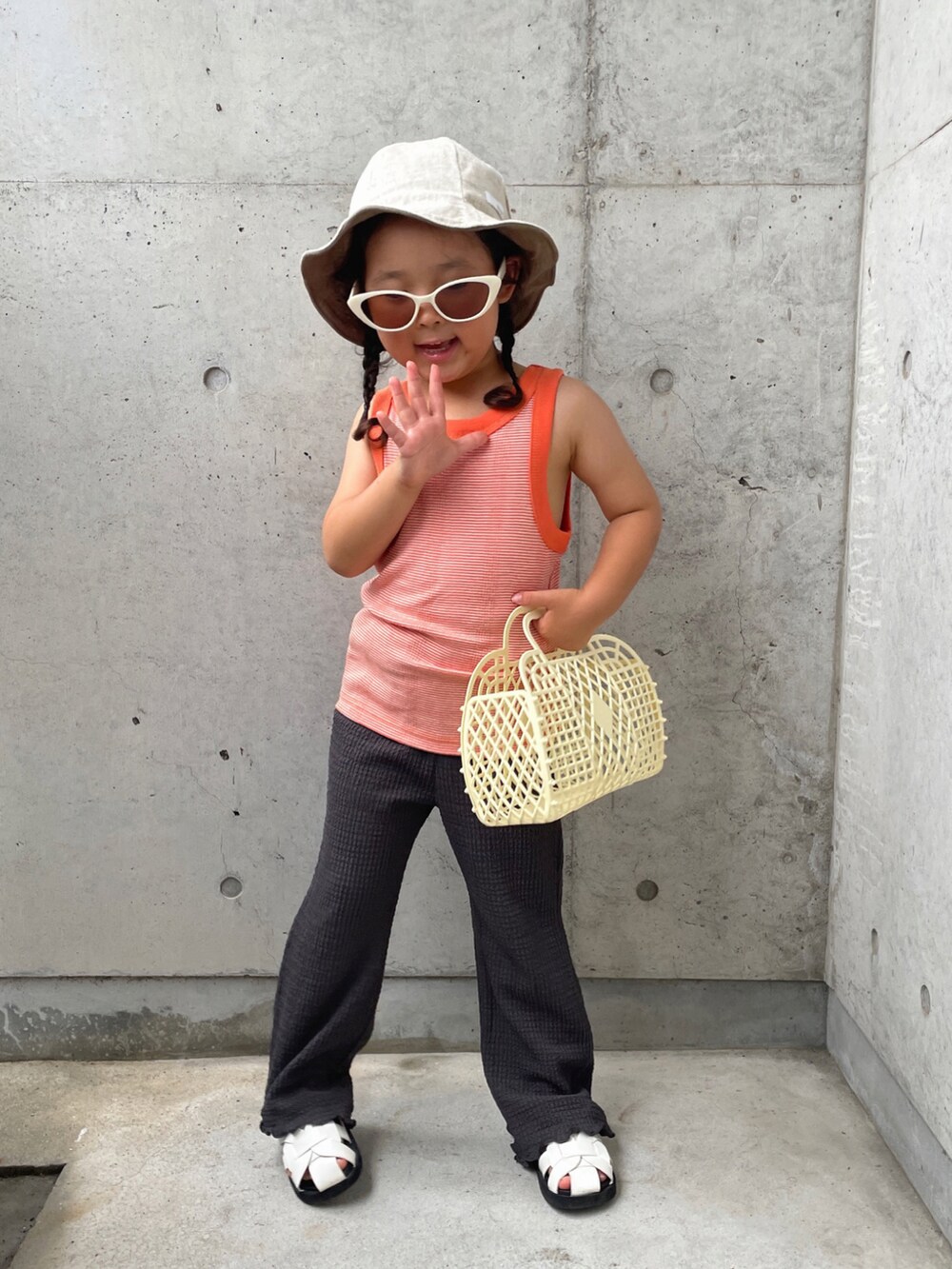 オレンジ系のタンクトップ、グレー系のその他パンツ、ホワイト系のバッグを着用したキッズの夏コーディネートの2枚目の写真