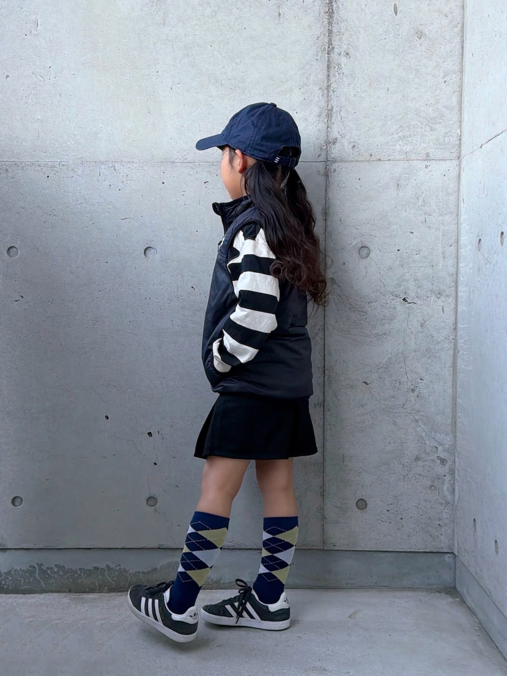 ブラック系のベスト、ホワイト系のポロシャツ、ベージュ系のスカートを着用したキッズの冬コーディネートの5枚目の写真