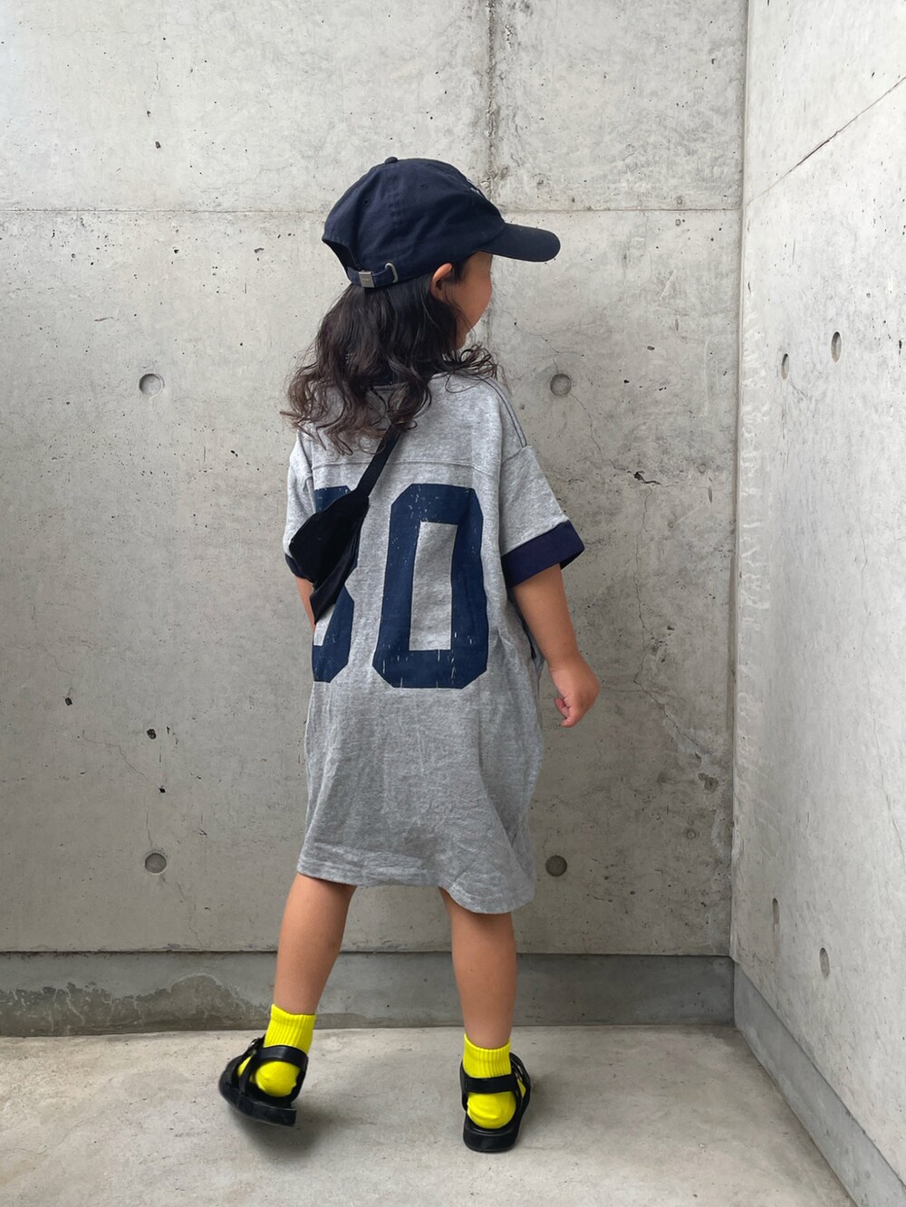 グレー系のワンピース、ブラック系のサンダル、ブルー系のキャップを着用したキッズの夏コーディネートの2枚目の写真