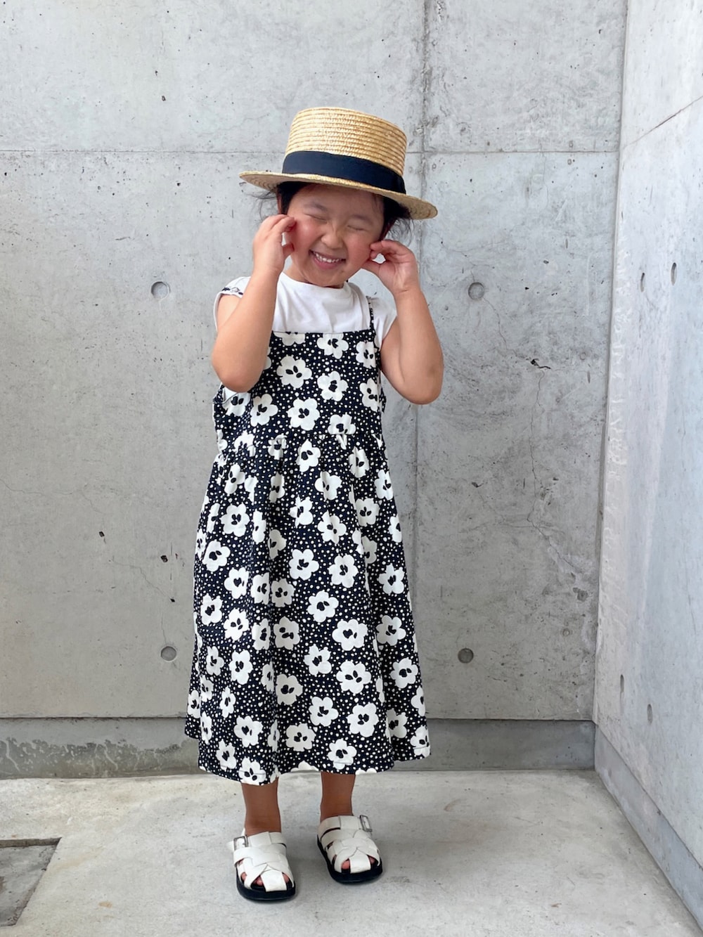 ブラック系のワンピース、ホワイト系のサンダル、ベージュ系のハットを着用したキッズの夏コーディネートの2枚目の写真