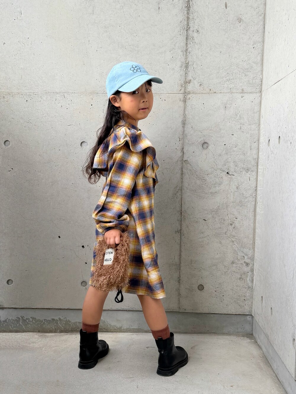 イエロー系のワンピース、ブラウン系のショルダーバッグ、ブラック系のブーツを着用したキッズの秋コーディネートの4枚目の写真