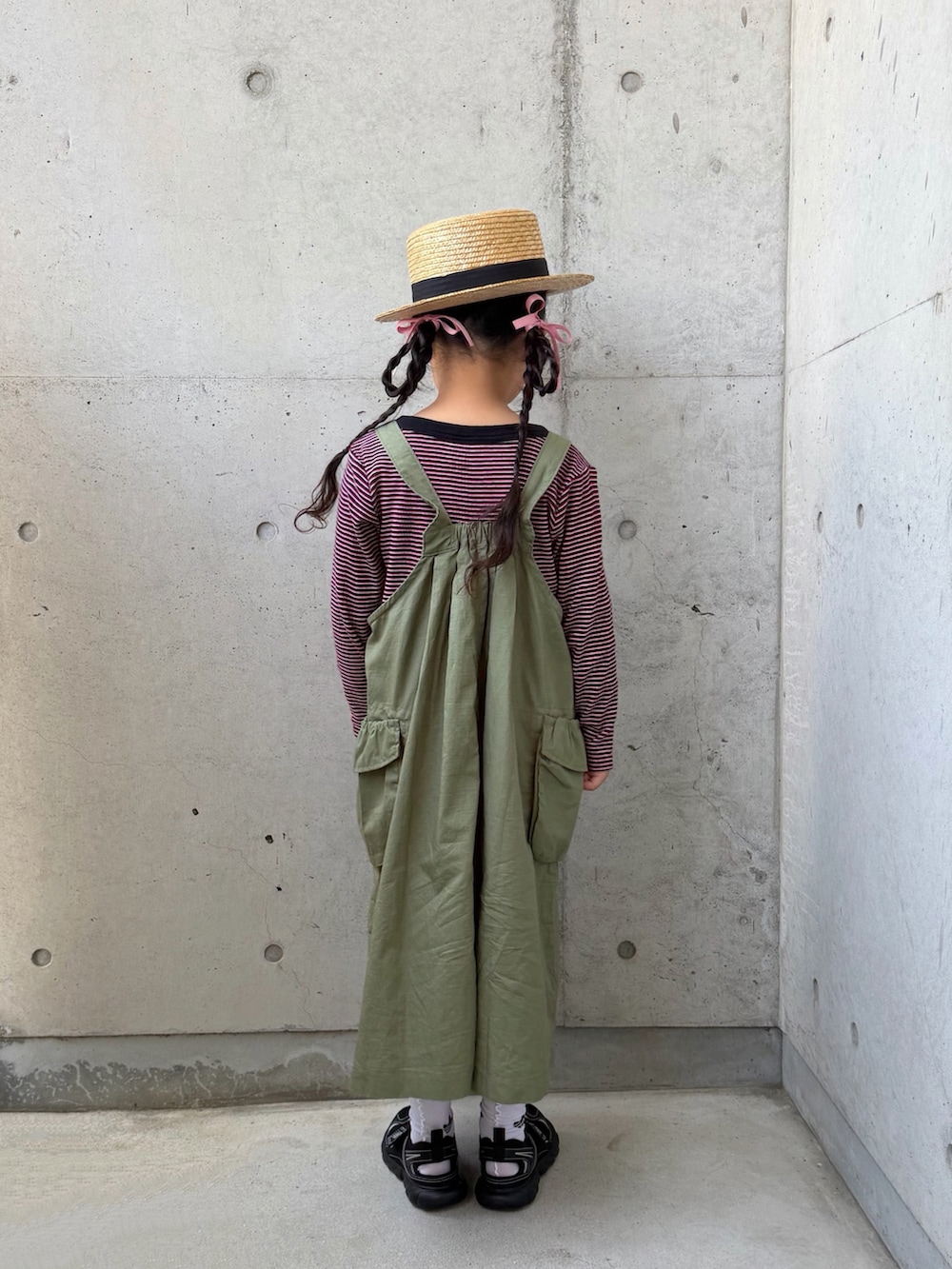 グリーン系のジャンパースカート、ブラック系のサンダル、レッド系のTシャツ/カットソーを着用したキッズの春コーディネートの5枚目の写真