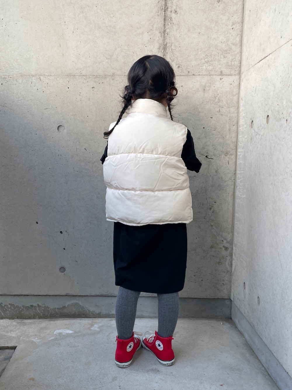 ホワイト系のダウンベスト、ブラック系のワンピース、レッド系のスニーカーを着用したキッズの秋コーディネートの3枚目の写真