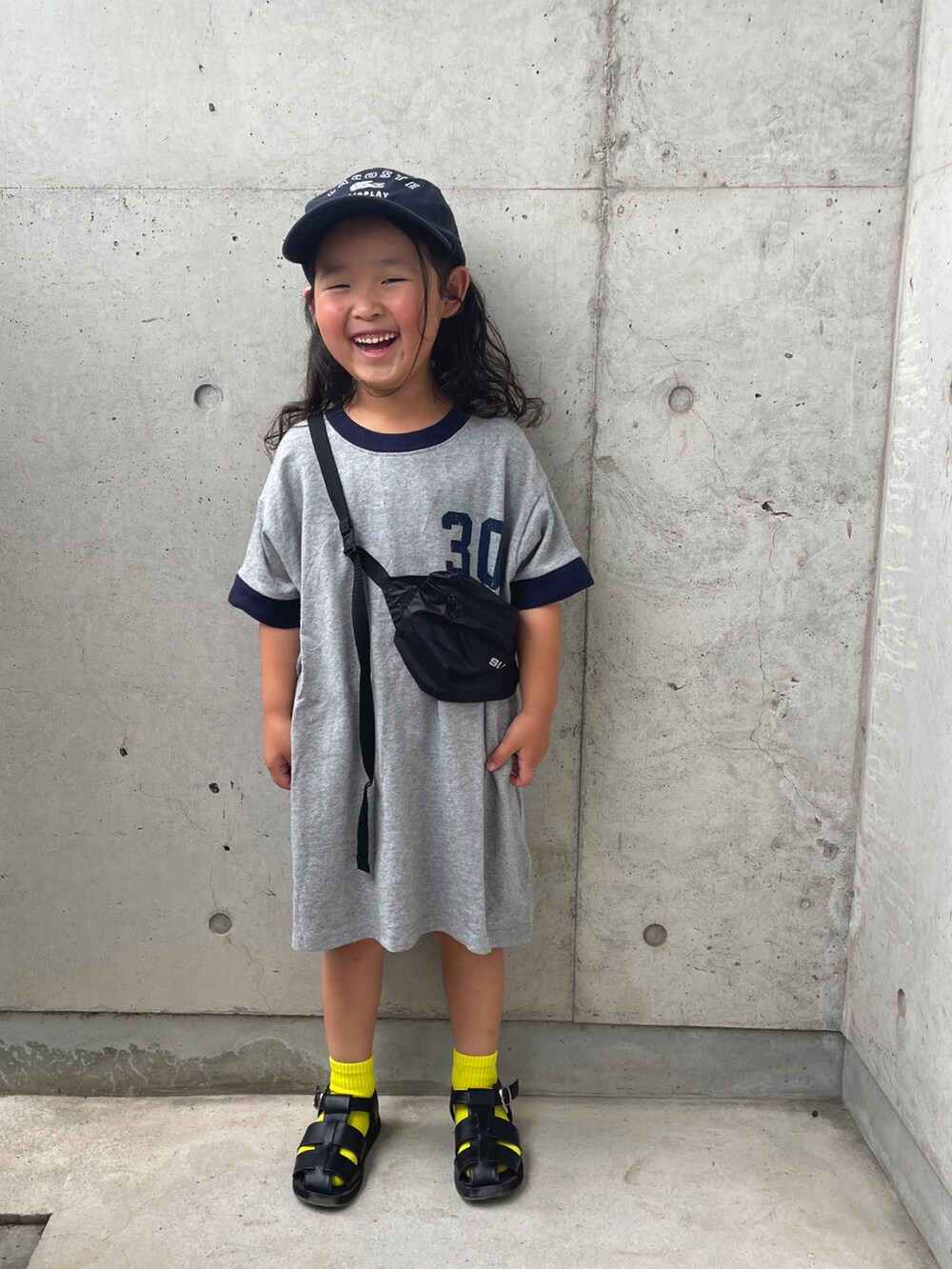 グレー系のワンピース、ブラック系のサンダル、ブルー系のキャップを着用したキッズの夏コーディネートの3枚目の写真