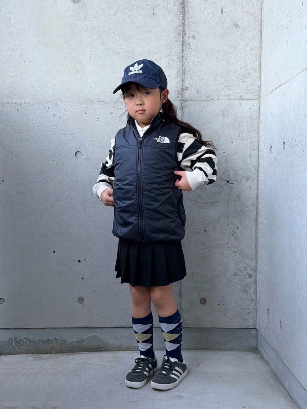 ブラック系のベスト、ホワイト系のポロシャツ、ベージュ系のスカートを着用したキッズの冬コーディネートの2枚目の写真