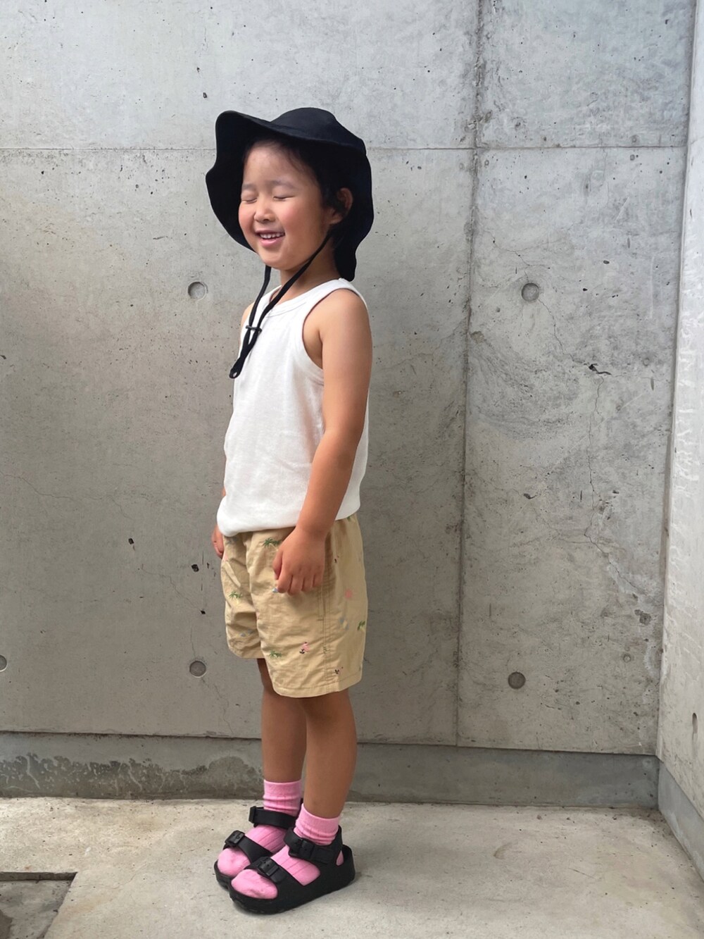 ホワイト系のタンクトップ、ベージュ系のパンツ、ブラック系のサンダルを着用したキッズの夏コーディネートの2枚目の写真