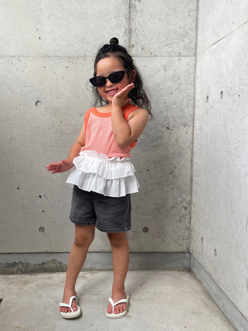 ホワイト系のサンダル、オレンジ系のタンクトップ、グレー系のパンツを着用したキッズの夏コーディネートの2枚目の写真