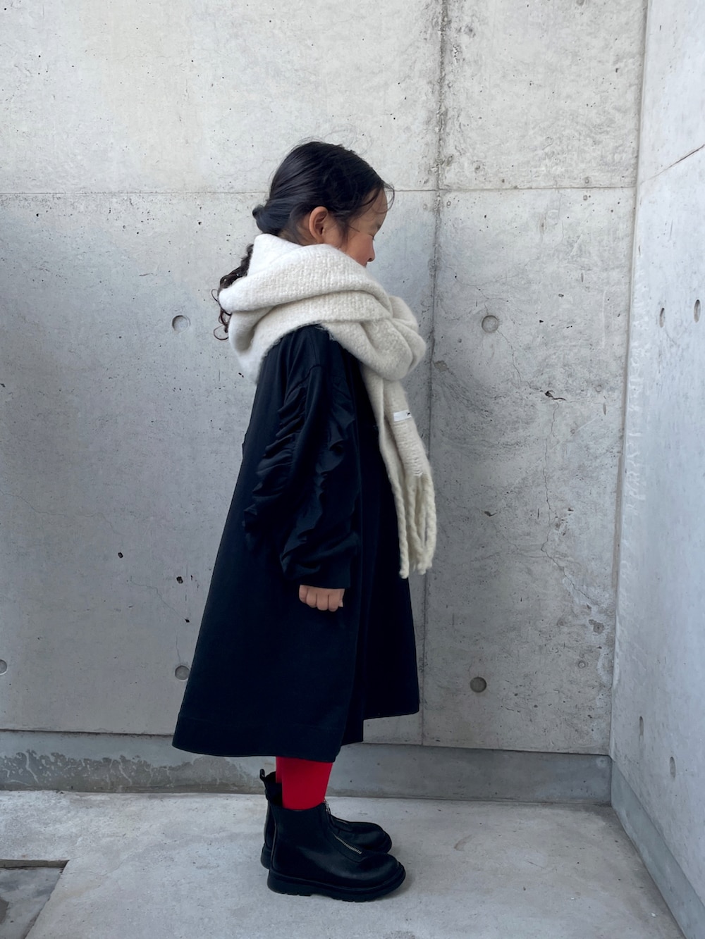 ブラック系のワンピース、ブラック系のブーツ、ホワイト系のマフラーを着用したキッズの冬コーディネートの4枚目の写真