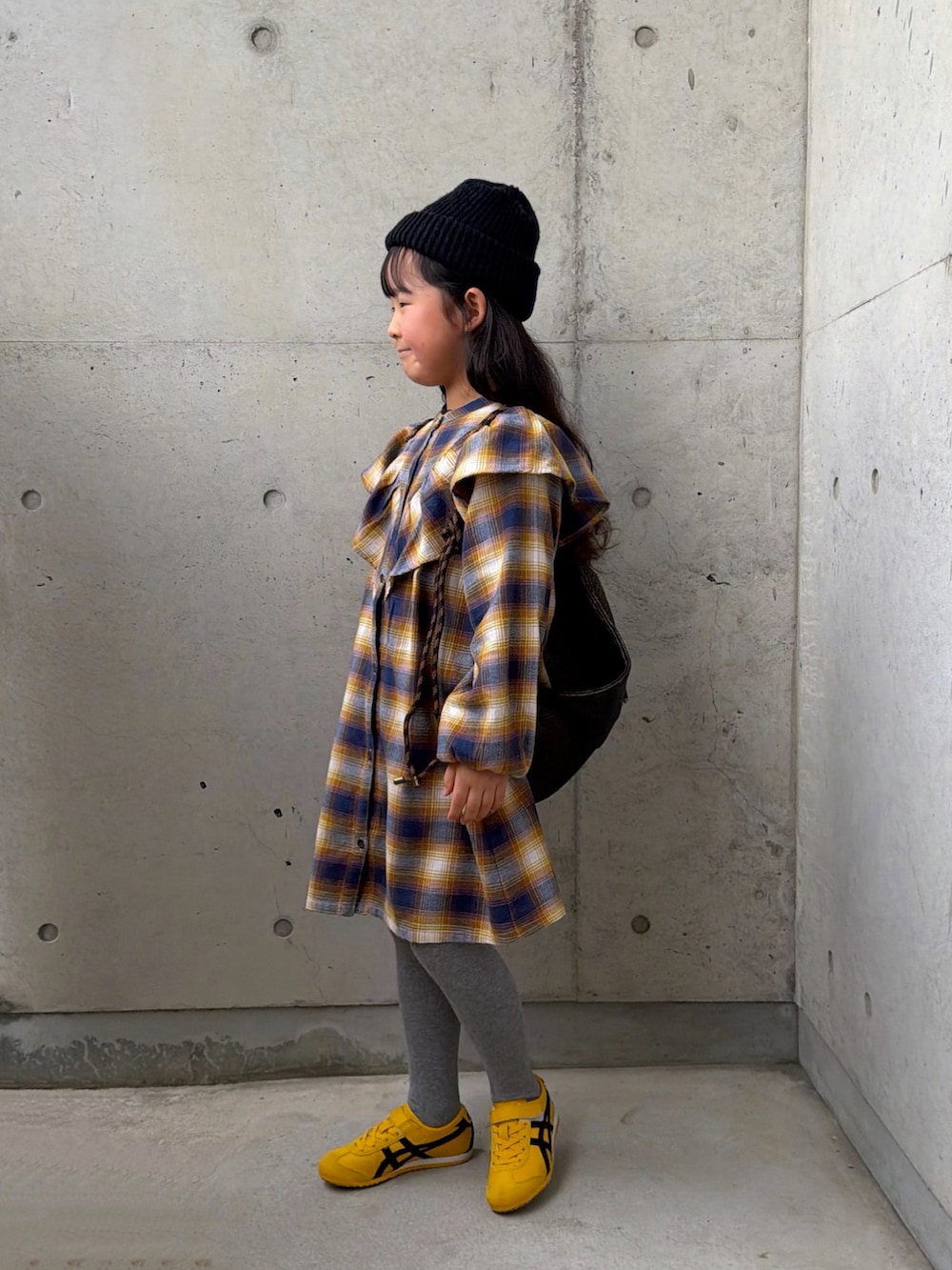 イエロー系のワンピース、イエロー系のスニーカー、ブラック系のバックパック/リュックを着用したキッズの春コーディネートの2枚目の写真