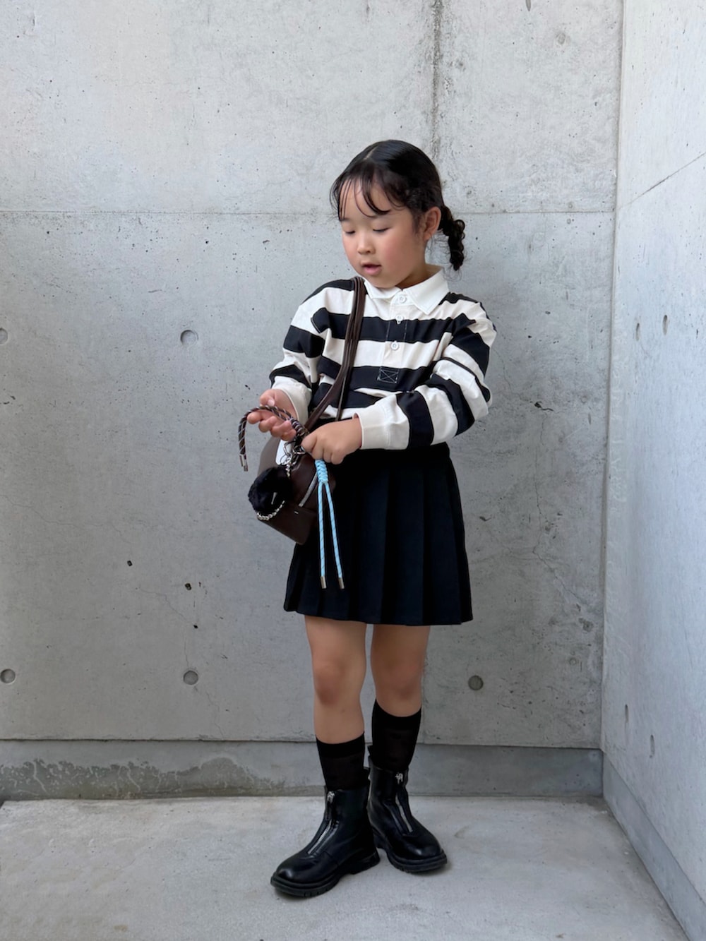 ブラウン系のショルダーバッグ、ブラック系のブーツ、ホワイト系のポロシャツを着用したキッズの秋コーディネートの5枚目の写真