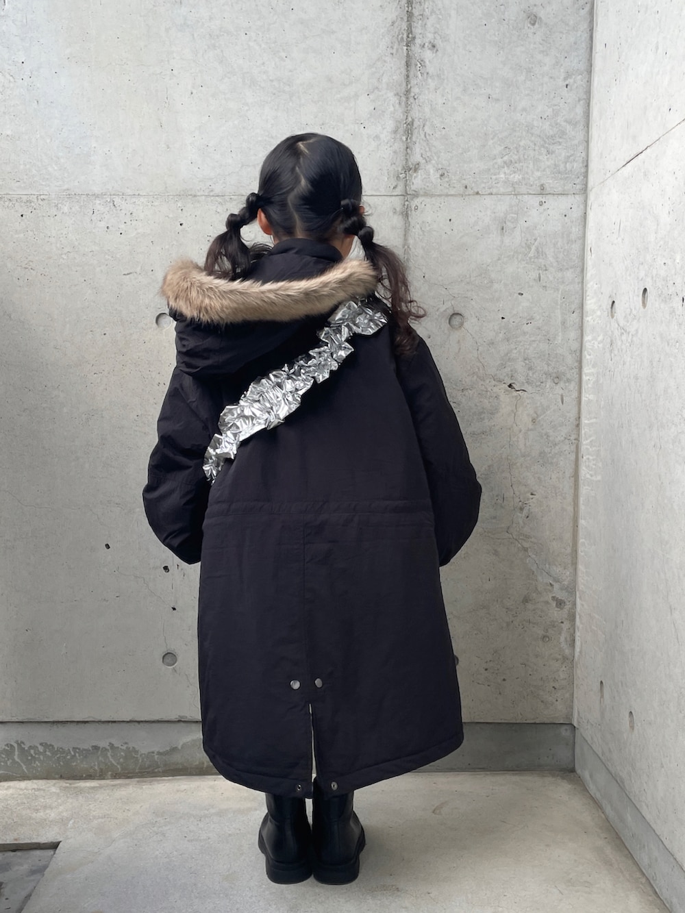 シルバー系のショルダーバッグ、ブラック系のミリタリージャケット、ブラック系のブーツを着用したキッズの冬コーディネートの3枚目の写真