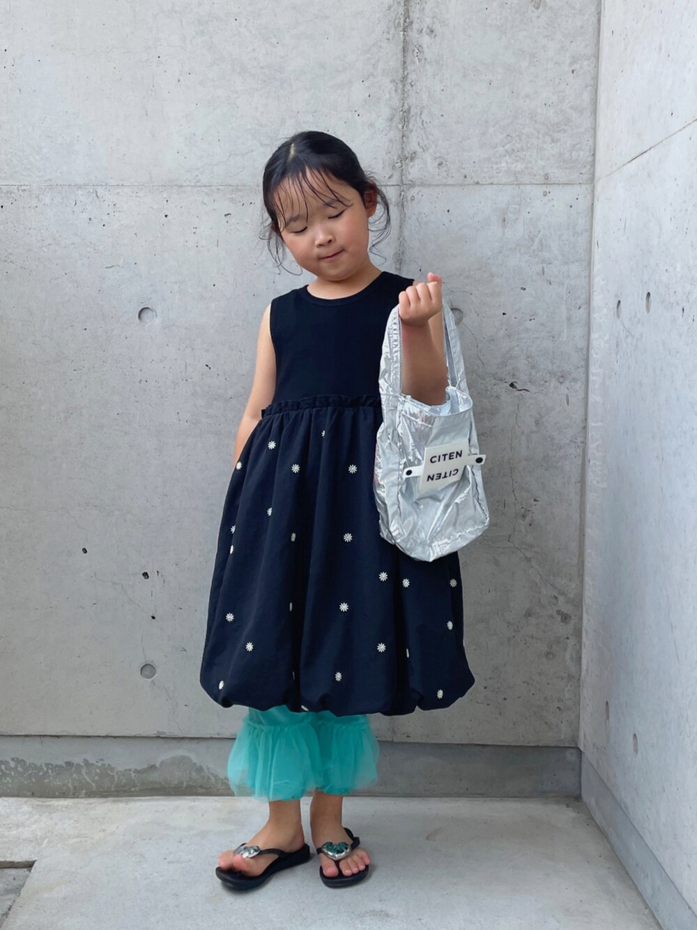 シルバー系のハンドバッグ、ブラック系のワンピース、ブラック系のサンダルを着用したキッズの夏コーディネートの4枚目の写真