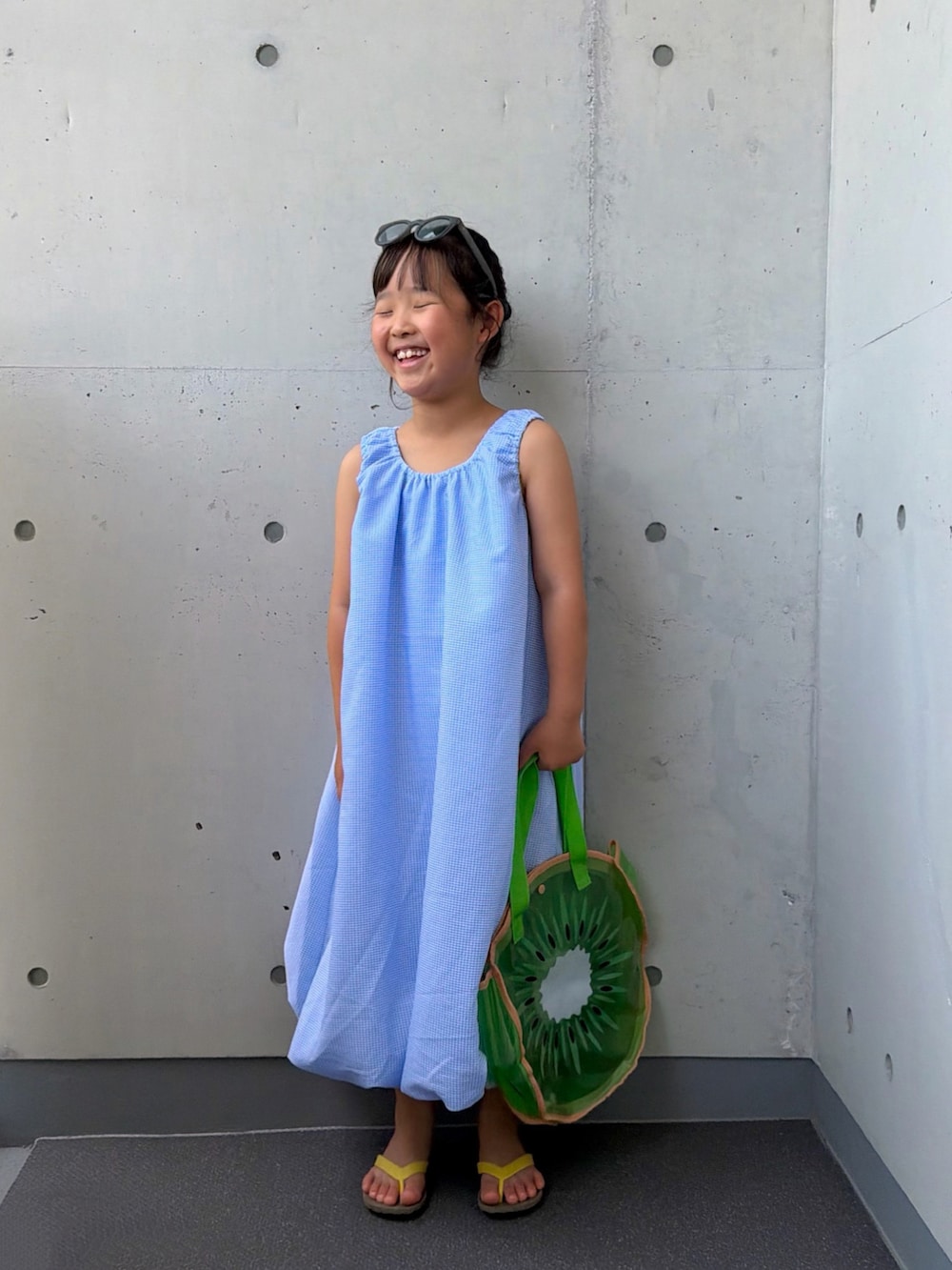 ブルー系のワンピース、グリーン系のトートバッグ、ブラウン系のサンダルを着用したキッズの夏コーディネートの2枚目の写真