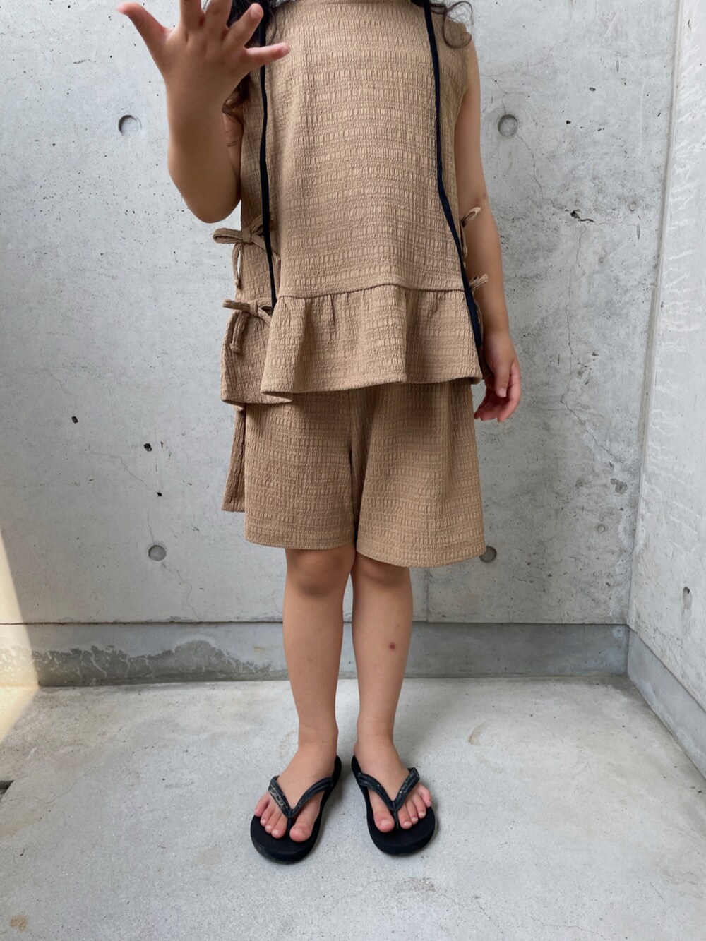 ブラウン系のパンツドレス、ブラック系のサンダル、ブラック系の帽子を着用したキッズの夏コーディネートの5枚目の写真