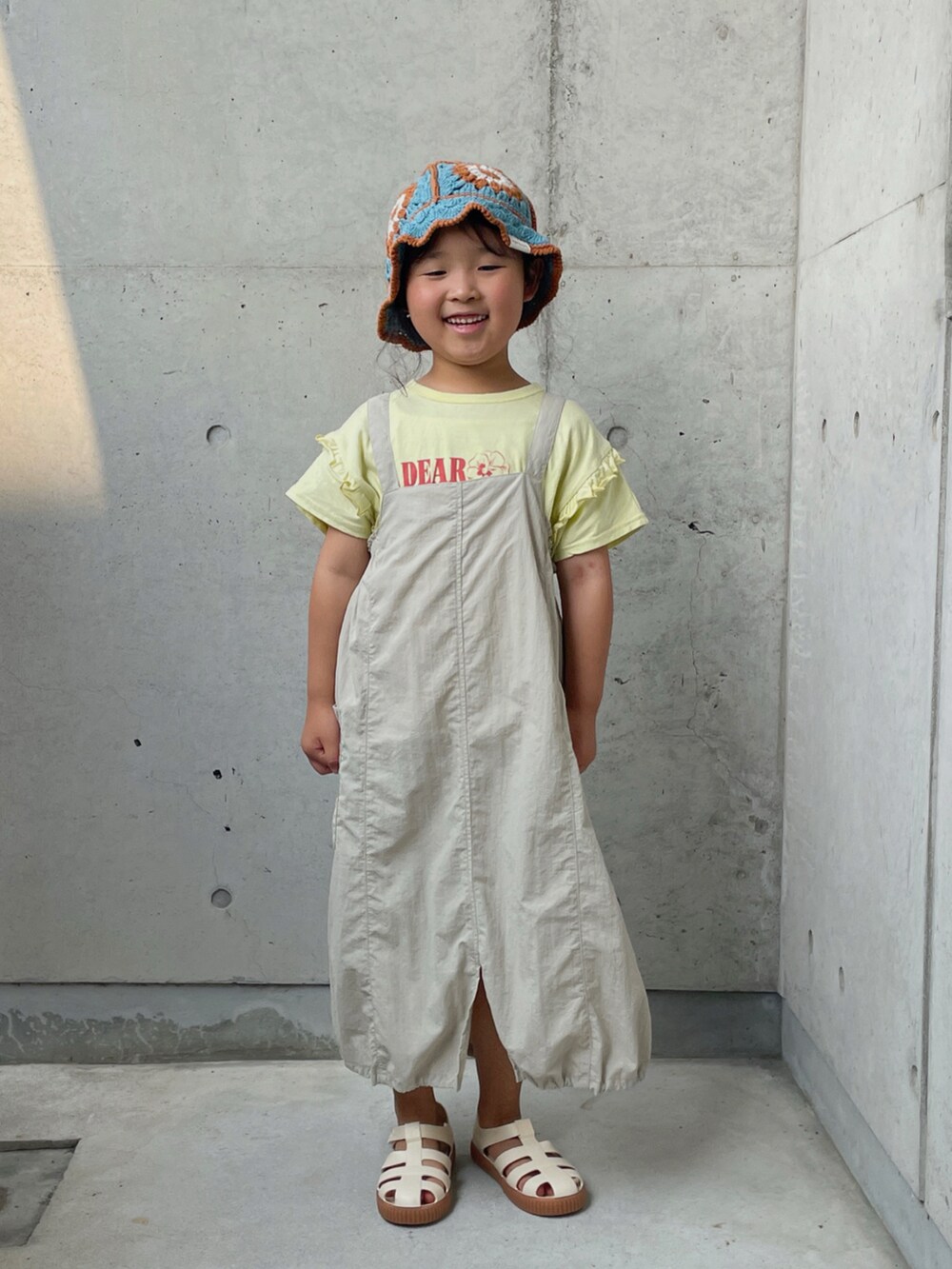 ベージュ系のTシャツ/カットソー、ベージュ系のワンピース、ホワイト系のサンダルを着用したキッズの夏コーディネートの5枚目の写真