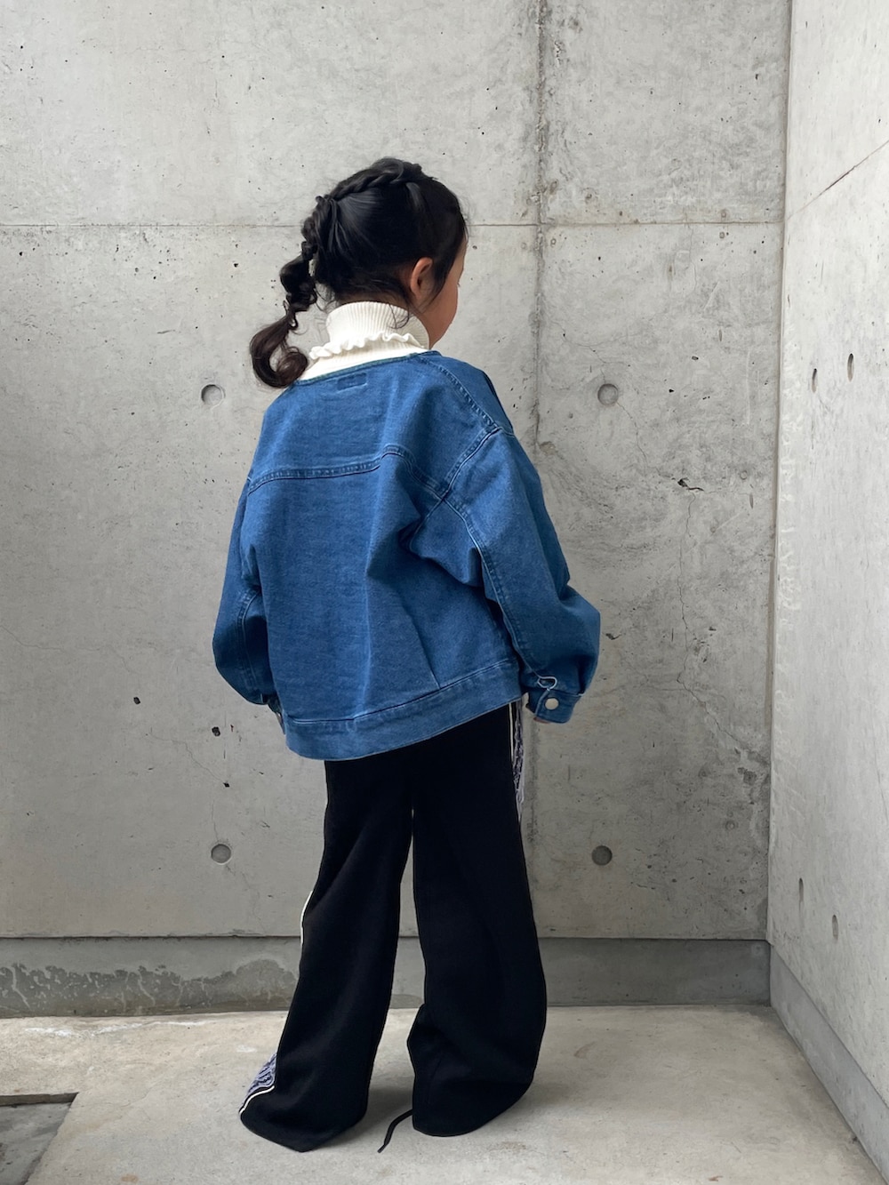 ブラック系のパンツ、ブルー系のデニムジャケット、ホワイト系のニット/セーターを着用したキッズの春コーディネートの2枚目の写真