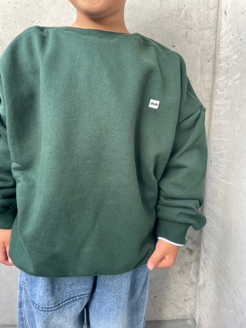 グリーン系のスウェット、ブルー系のデニムパンツ、ホワイト系のスニーカーを着用したキッズの秋コーディネートの5枚目の写真