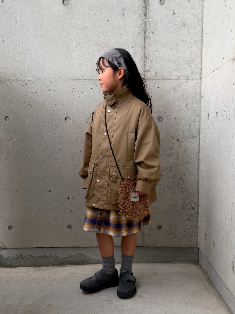 ベージュ系のミリタリージャケット、イエロー系のワンピース、グレー系のその他シューズを着用したキッズの冬コーディネートの2枚目の写真