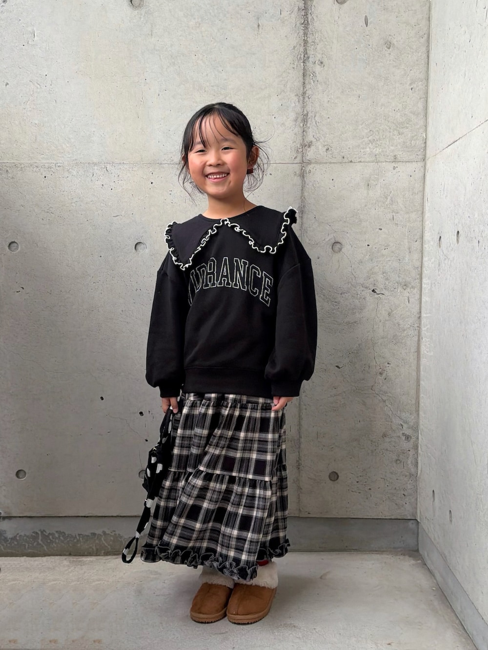 ブラック系のスウェット、ブラウン系のスカート、ブラック系のショルダーバッグを着用したキッズの秋コーディネートの2枚目の写真