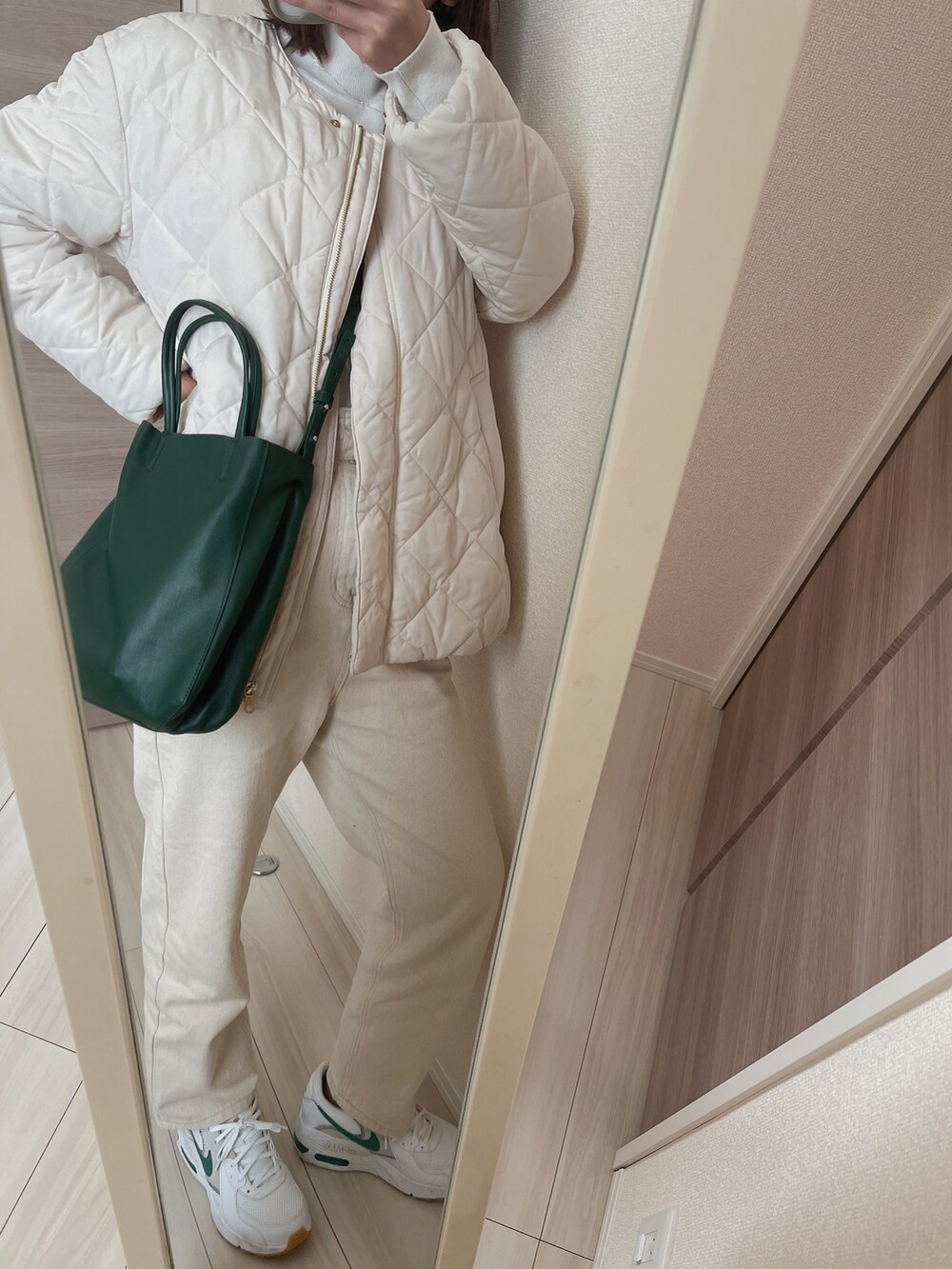 グリーン系のショルダーバッグ、ホワイト系のスニーカー、ベージュ系のデニムパンツを着用したレディースの冬コーディネートの2枚目の写真