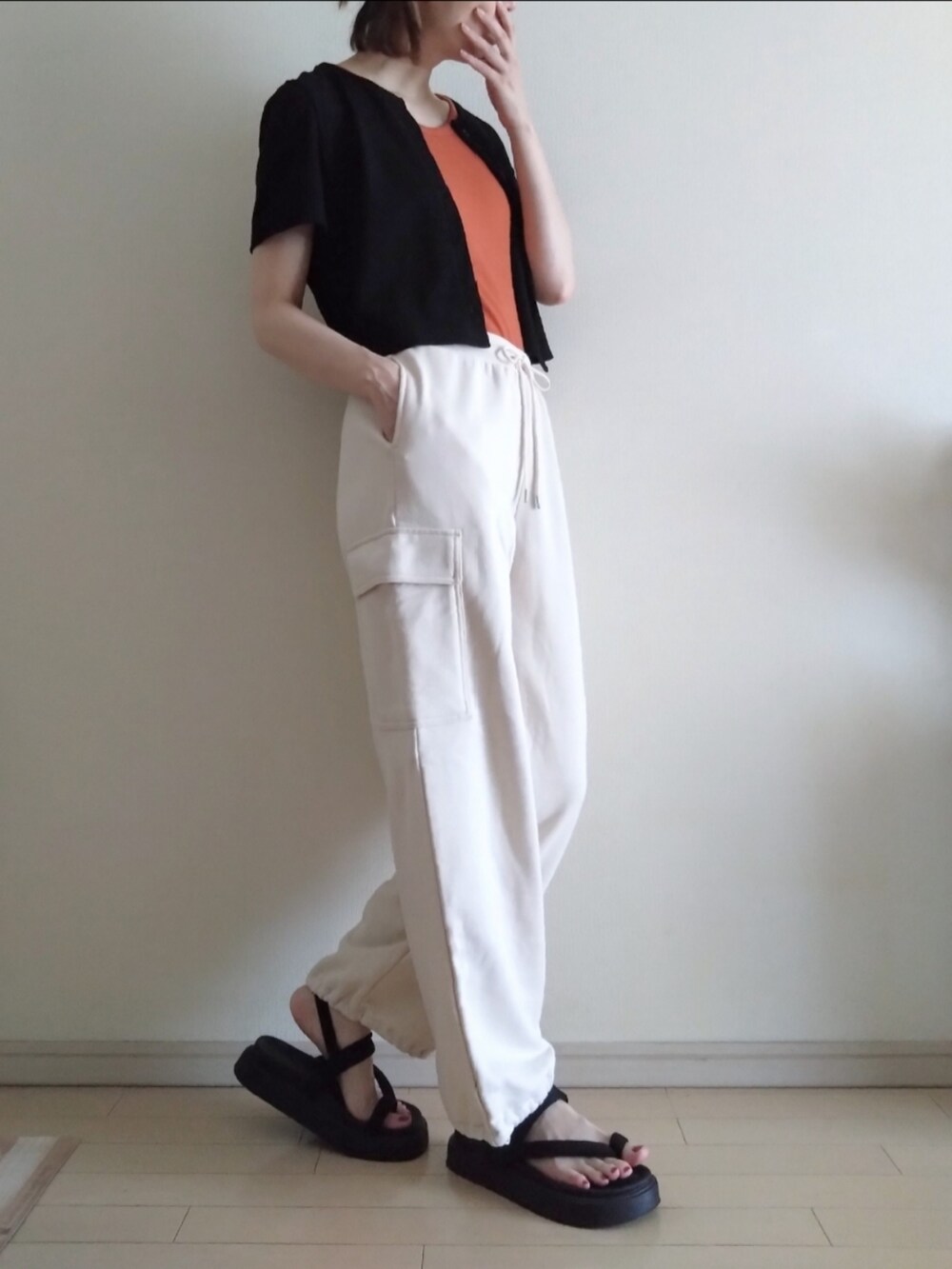 オレンジ系のタンクトップ、ブラック系のカーディガン/ボレロ、ホワイト系のカーゴパンツを着用したレディースの夏コーディネートの2枚目の写真