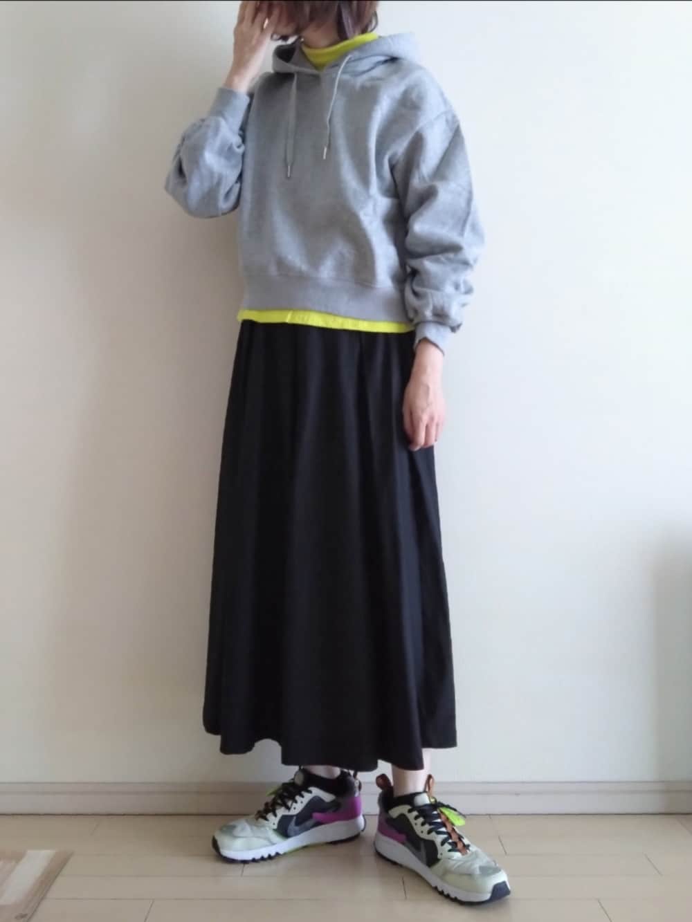 グレー系のパーカー、イエロー系のTシャツ/カットソー、ブラック系のスカートを着用したレディースの秋コーディネートの2枚目の写真