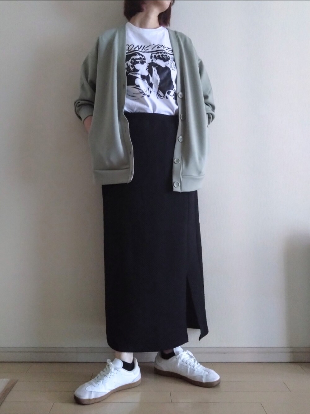 グリーン系のカーディガン/ボレロ、ホワイト系のTシャツ/カットソー、ブラック系のスカートを着用したレディースの秋コーディネートの2枚目の写真
