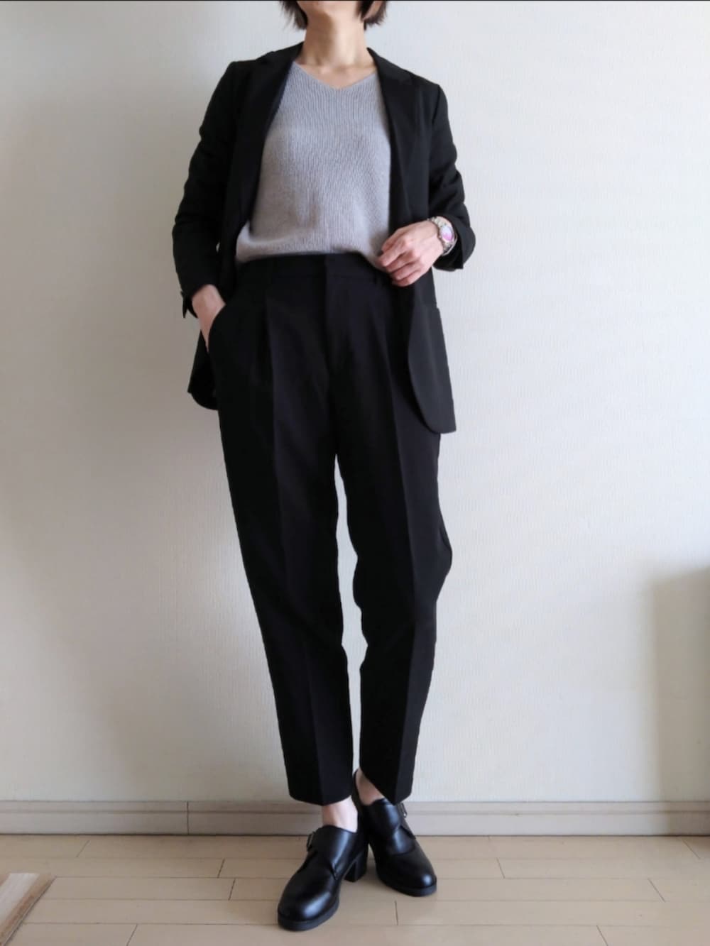 ブラック系のテーラードジャケット、グレー系のニット/セーター、ブラック系のスラックスを着用したレディースの春コーディネートの3枚目の写真