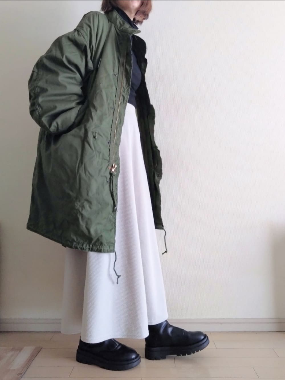 グリーン系のモッズコート、ブラック系のTシャツ/カットソー、グレー系のスカートを着用したレディースの冬コーディネートの2枚目の写真