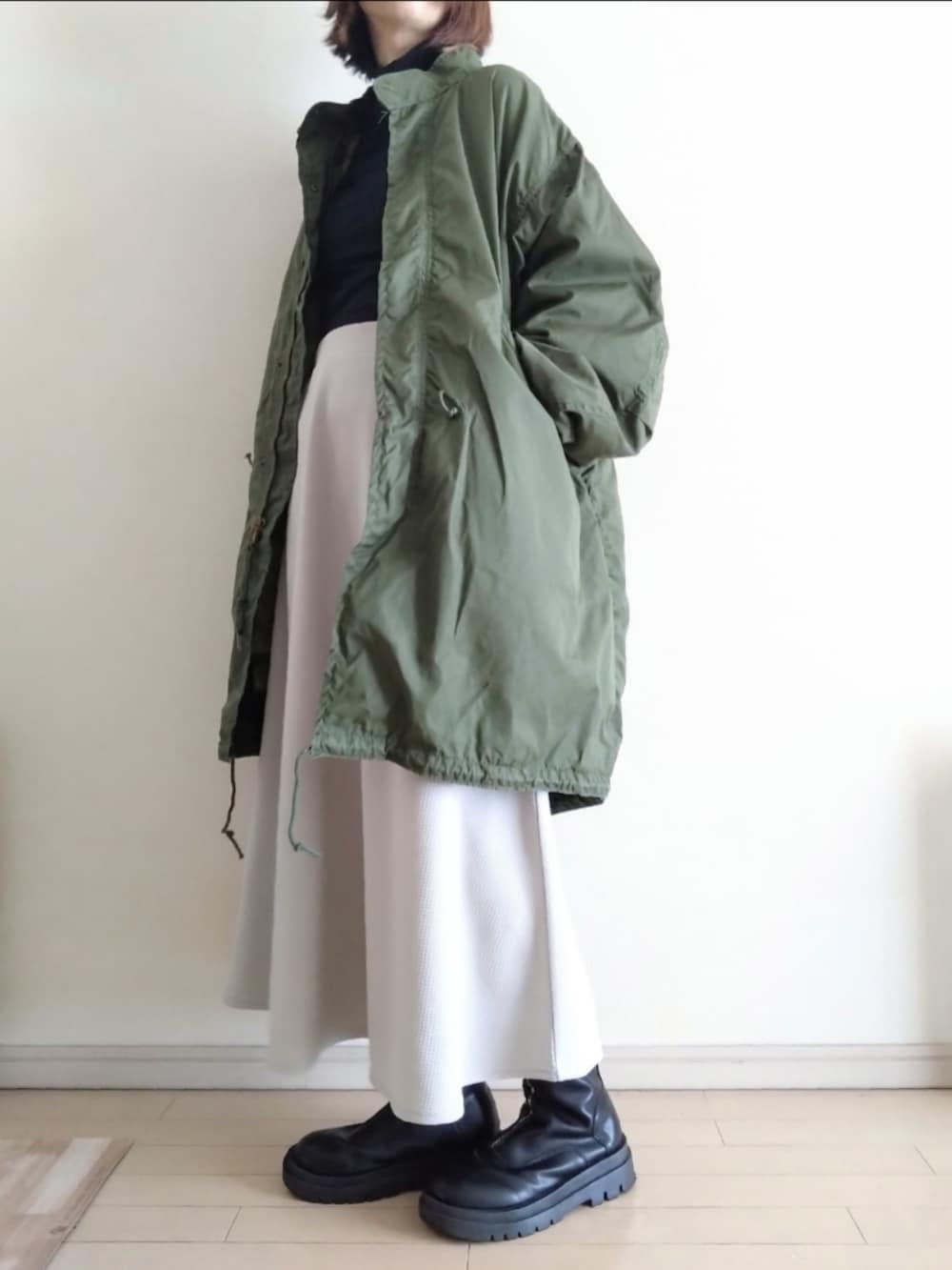 グリーン系のモッズコート、ブラック系のTシャツ/カットソー、グレー系のスカートを着用したレディースの冬コーディネートの3枚目の写真