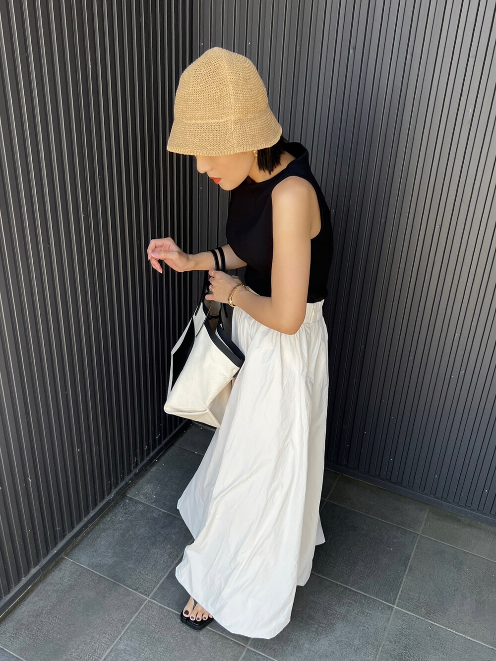 ブラック系のトートバッグ、ホワイト系のスカート、ブラック系のサンダルを着用したレディースの春コーディネートの2枚目の写真