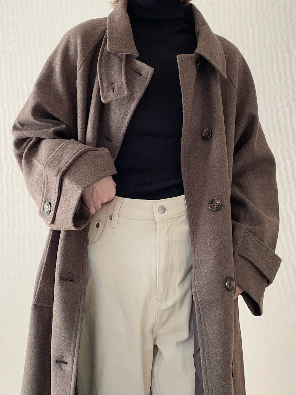 ブラウン系のステンカラーコート、ブラック系のニット/セーター、ホワイト系のその他パンツを着用したレディースの秋コーディネートの3枚目の写真