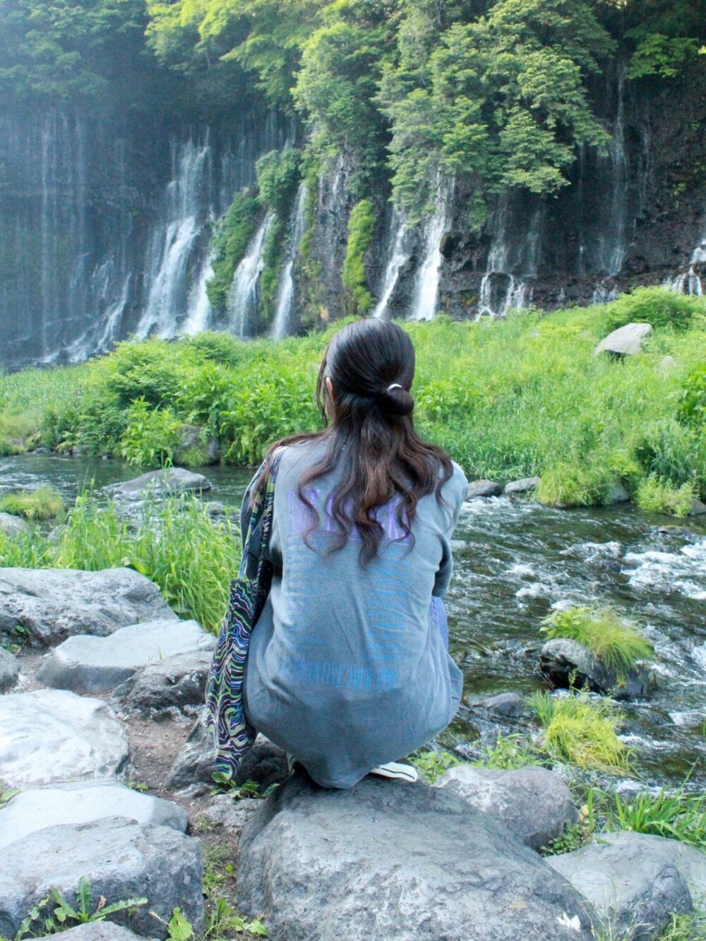 グリーン系のトートバッグ、グレー系のTシャツ/カットソー、パープル系のデニムパンツを着用したレディースの夏コーディネートの2枚目の写真