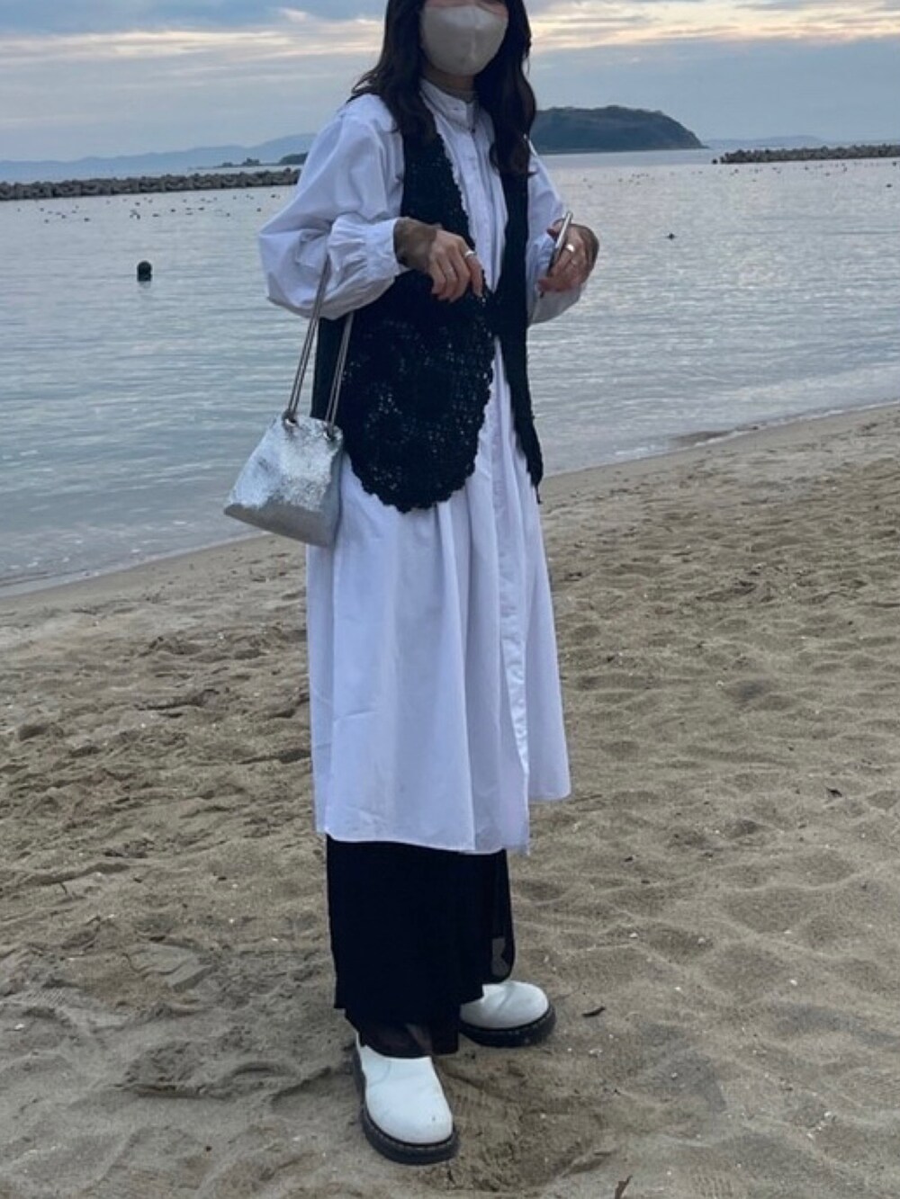 ブラック系のベスト、ホワイト系のシャツワンピース、シルバー系のショルダーバッグを着用したレディースの冬コーディネートの2枚目の写真