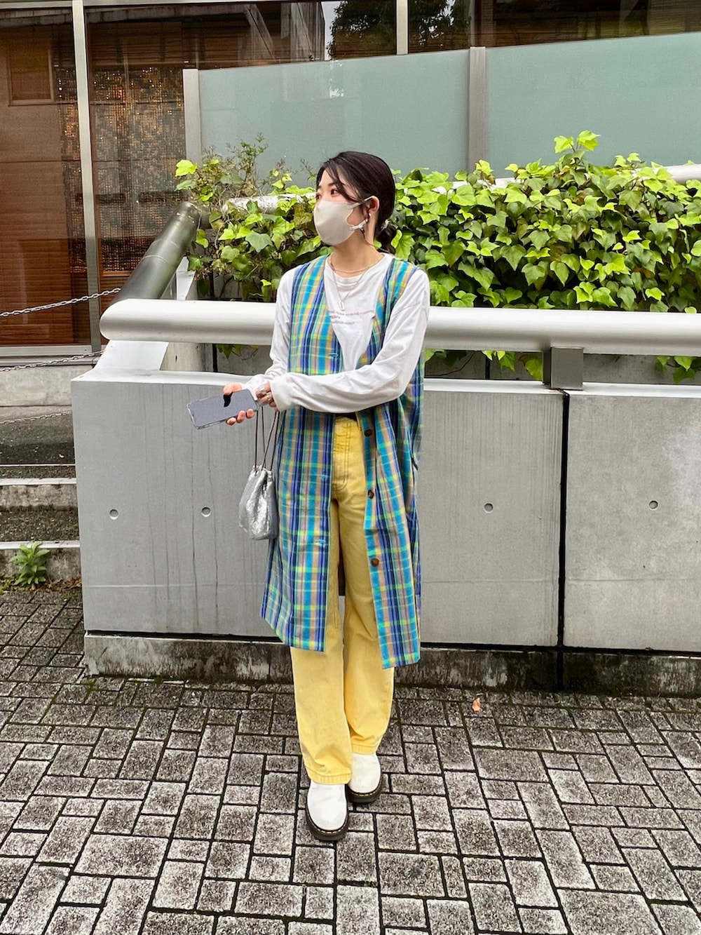 イエロー系のデニムパンツ、グリーン系のベスト、シルバー系のショルダーバッグを着用したレディースの春コーディネートの2枚目の写真