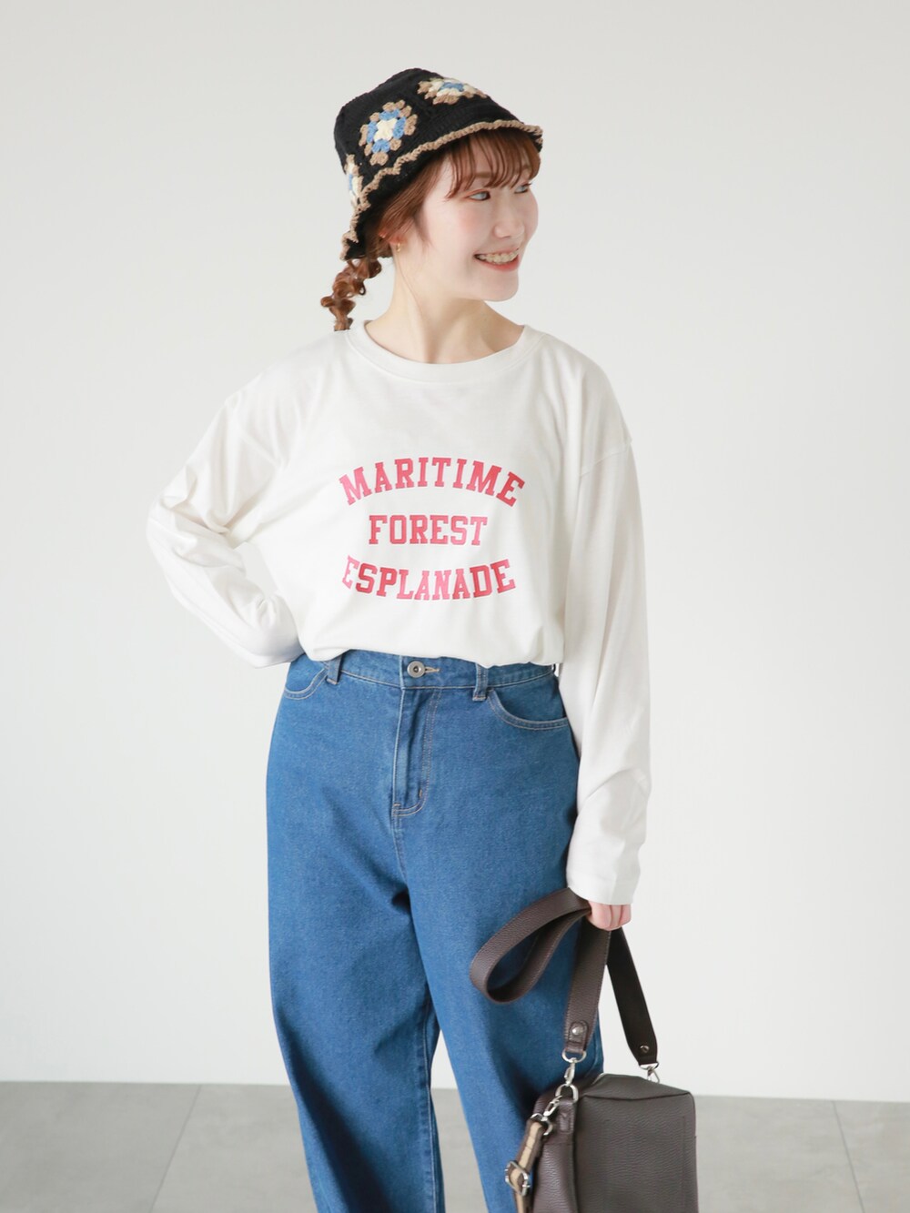 ブルー系のデニムパンツ、ブラウン系のハンドバッグ、ホワイト系のTシャツ/カットソーを着用したレディースの春コーディネートの2枚目の写真