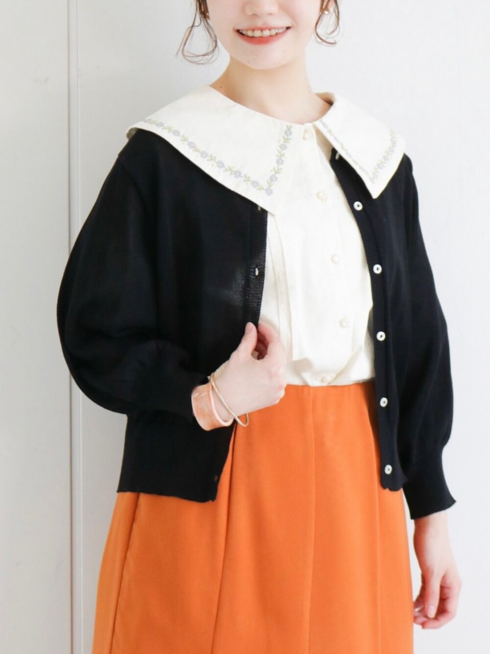 オレンジ系のスカート、ブラック系のカーディガン/ボレロ、ホワイト系のシャツ/ブラウスを着用したレディースの春コーディネートの2枚目の写真