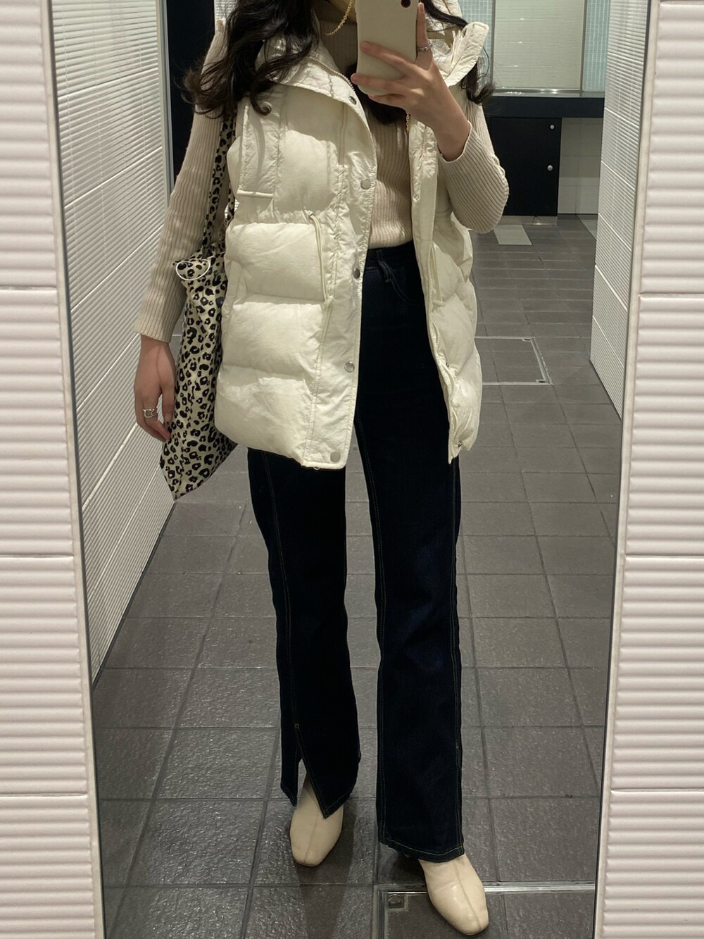 ホワイト系のダウンベスト、ホワイト系のニット/セーター、ブルー系のデニムパンツを着用したレディースの冬コーディネートの2枚目の写真