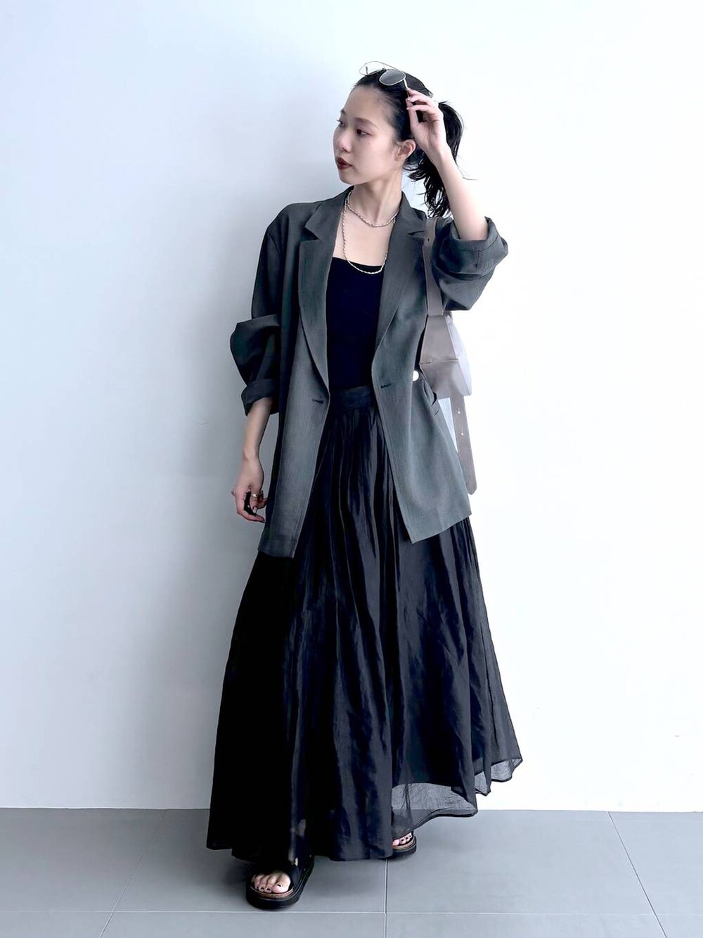 グレー系のテーラードジャケット、ブラック系のキャミソール、グリーン系のショルダーバッグを着用したレディースの夏コーディネートの3枚目の写真