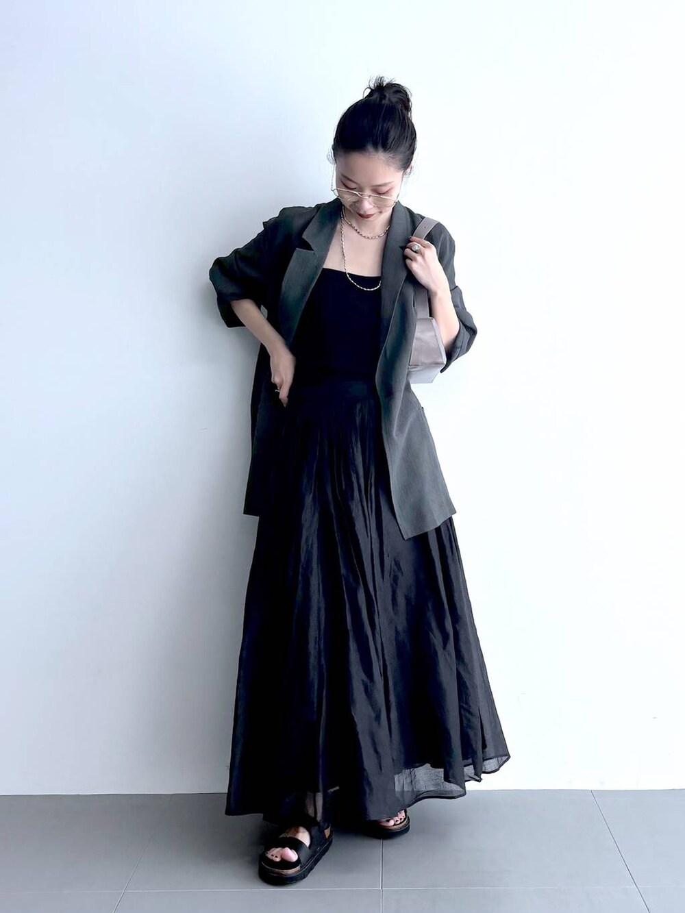 グレー系のテーラードジャケット、ブラック系のキャミソール、グリーン系のショルダーバッグを着用したレディースの夏コーディネートの2枚目の写真